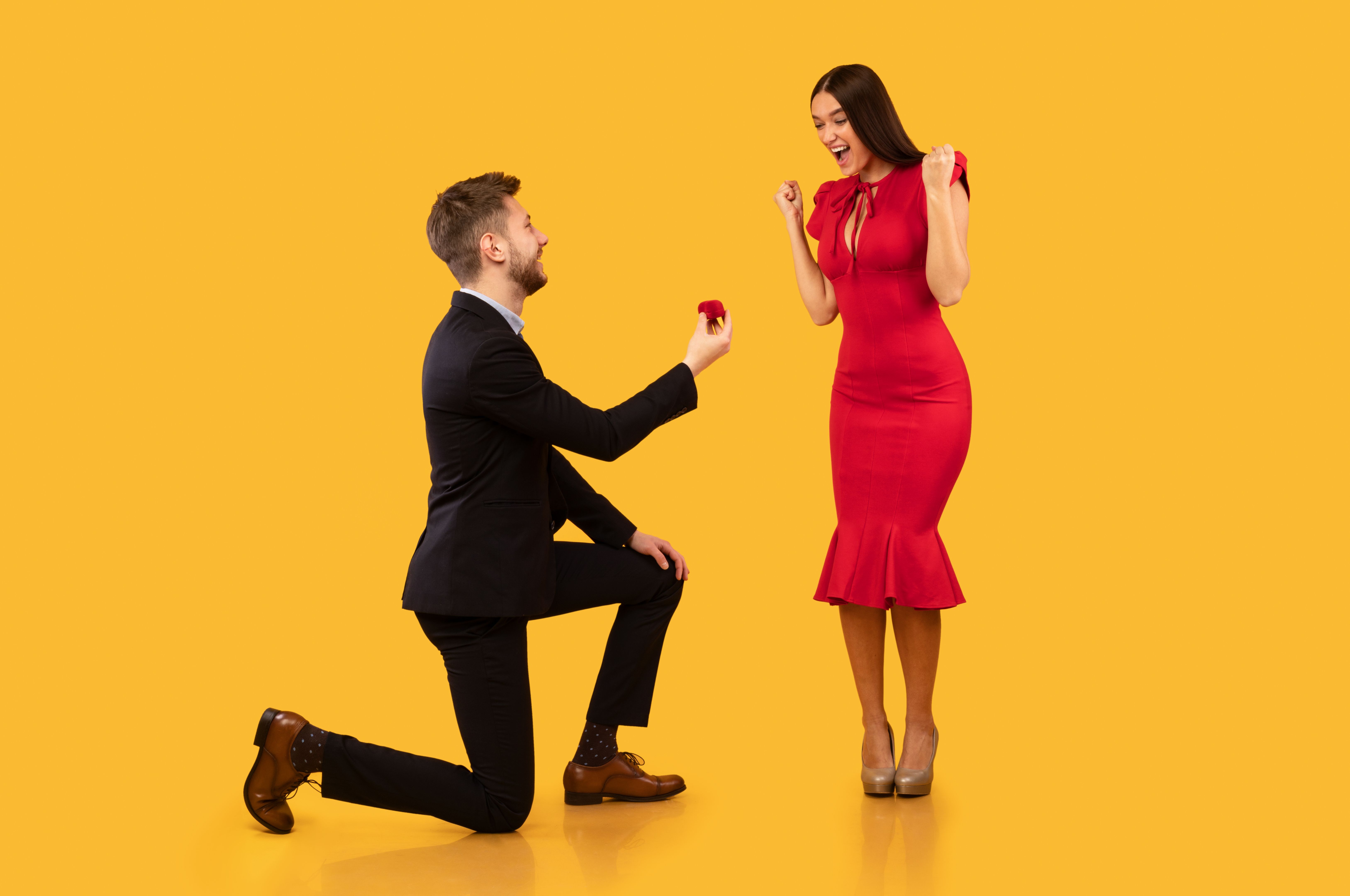 Young Man Proposing To Girlfriend Offering Ring Standing In Studio