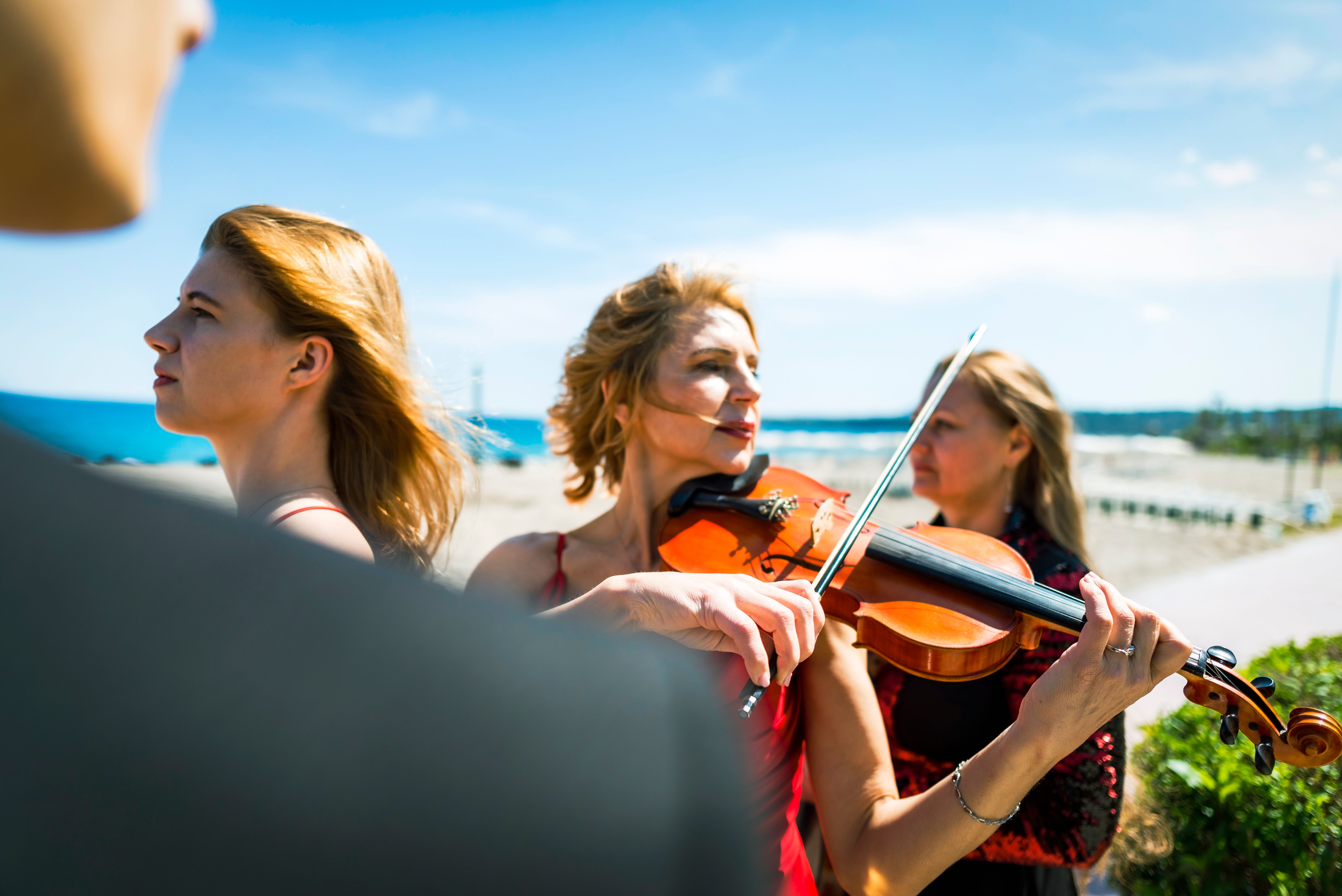 Three musicians in red dress and one musician in black suit at the beach.