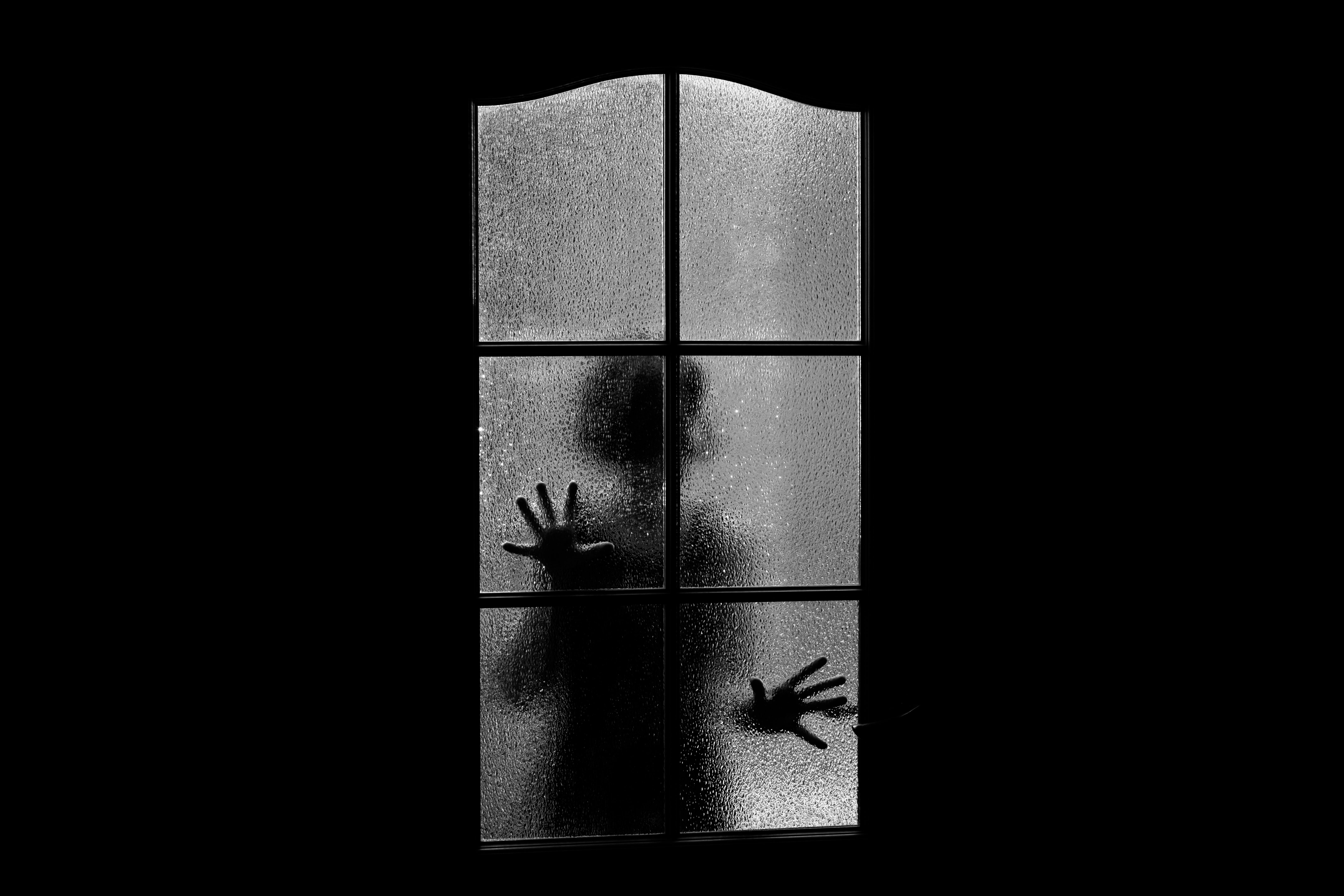 Dark silhouette of girl behind glass. Locked alone in room behind door on Halloween in grayscale. Nightmare of child with aliens, monsters and ghosts. Evil in home in monochrome. Inside haunted house.