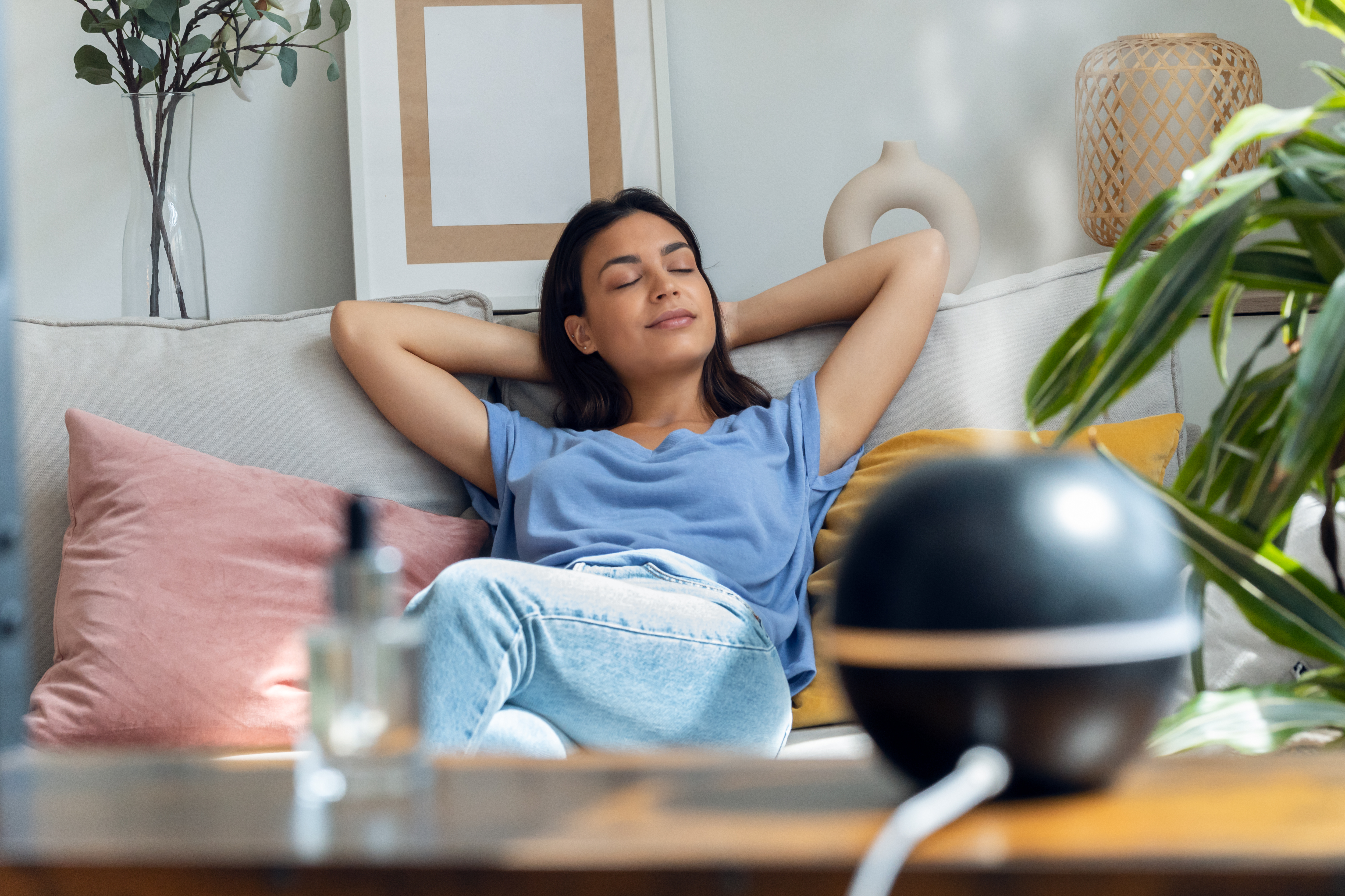 Beautiful woman relaxing on a coach while essential oil aroma diffuser humidifier the air in living room at home