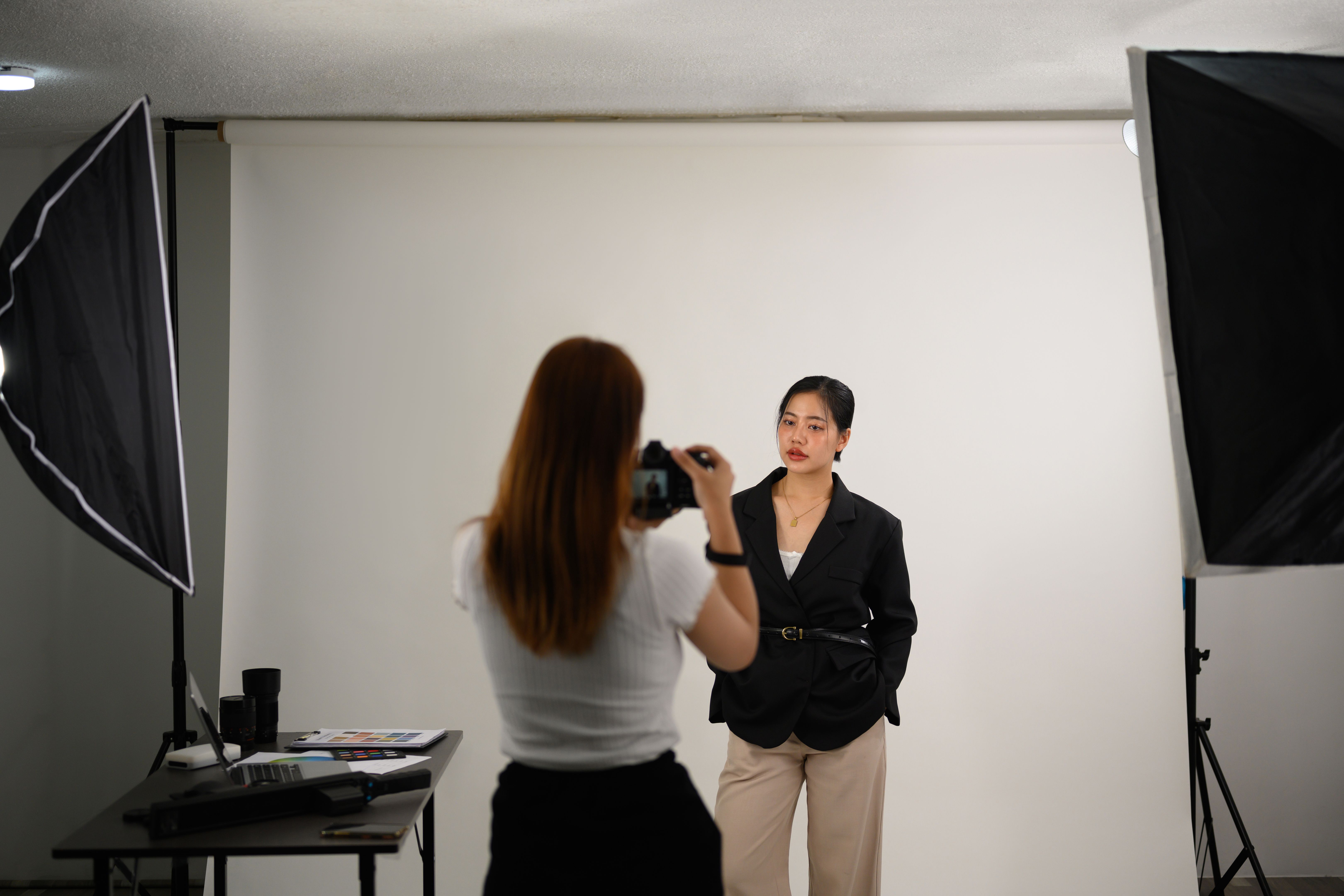 Fashion photographer taking picture of young female model in lighting studio