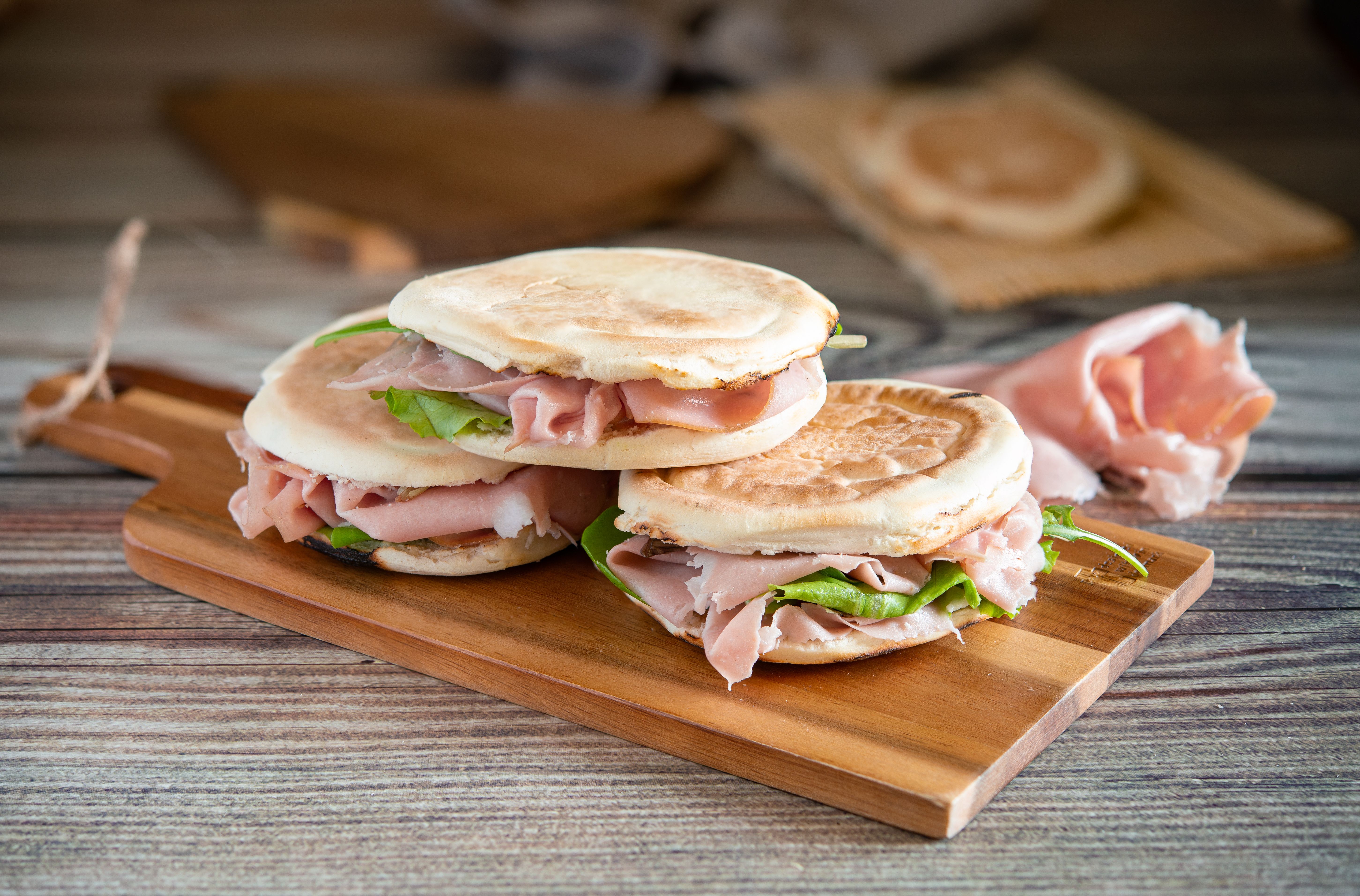 Stack of crescentine tigelle with mortadella and rocket on wooden board