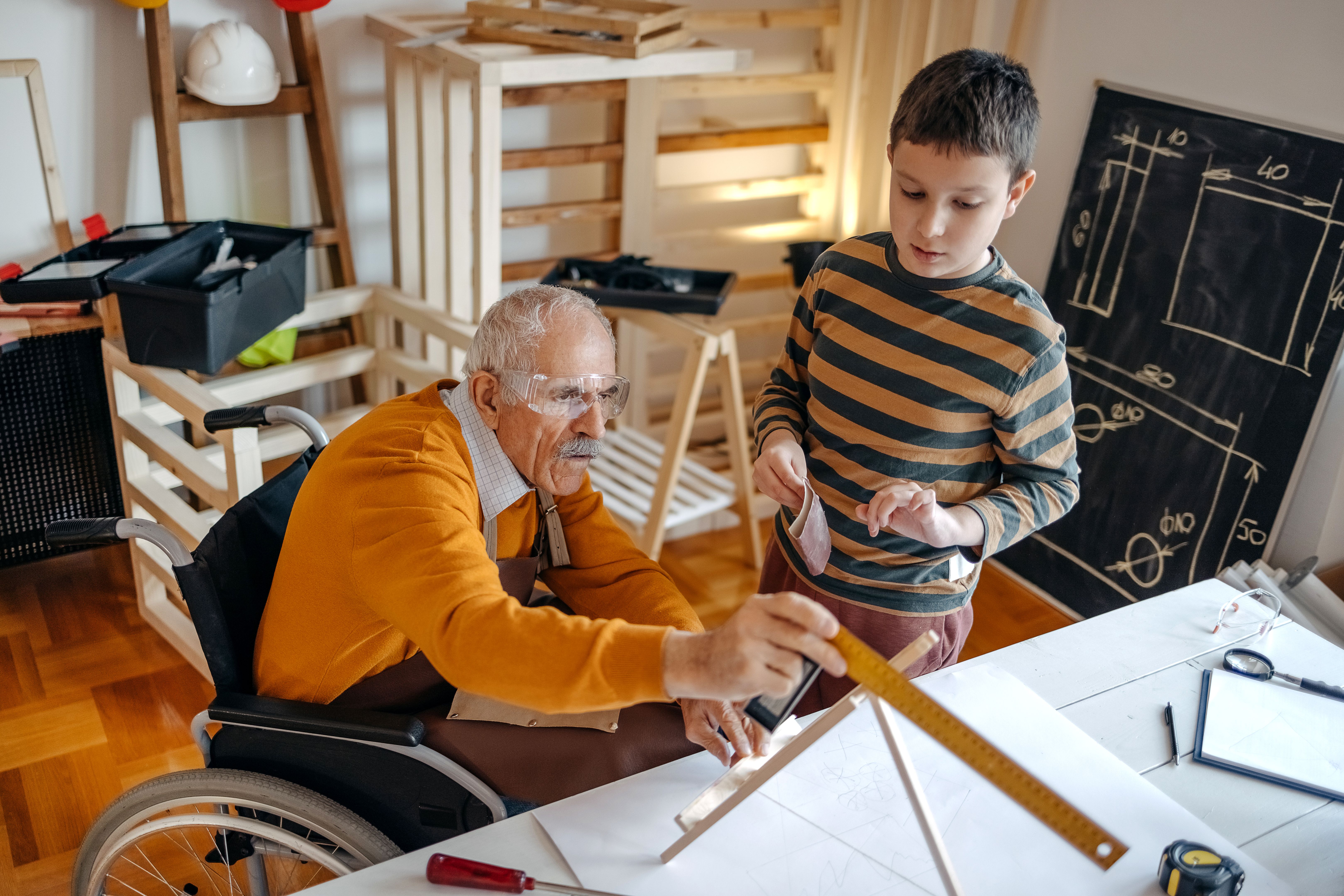 Boy helping grandfather in wheelchair in his carpentry workshop Boy helping grandfather in wheelchair in his carpentry workshop