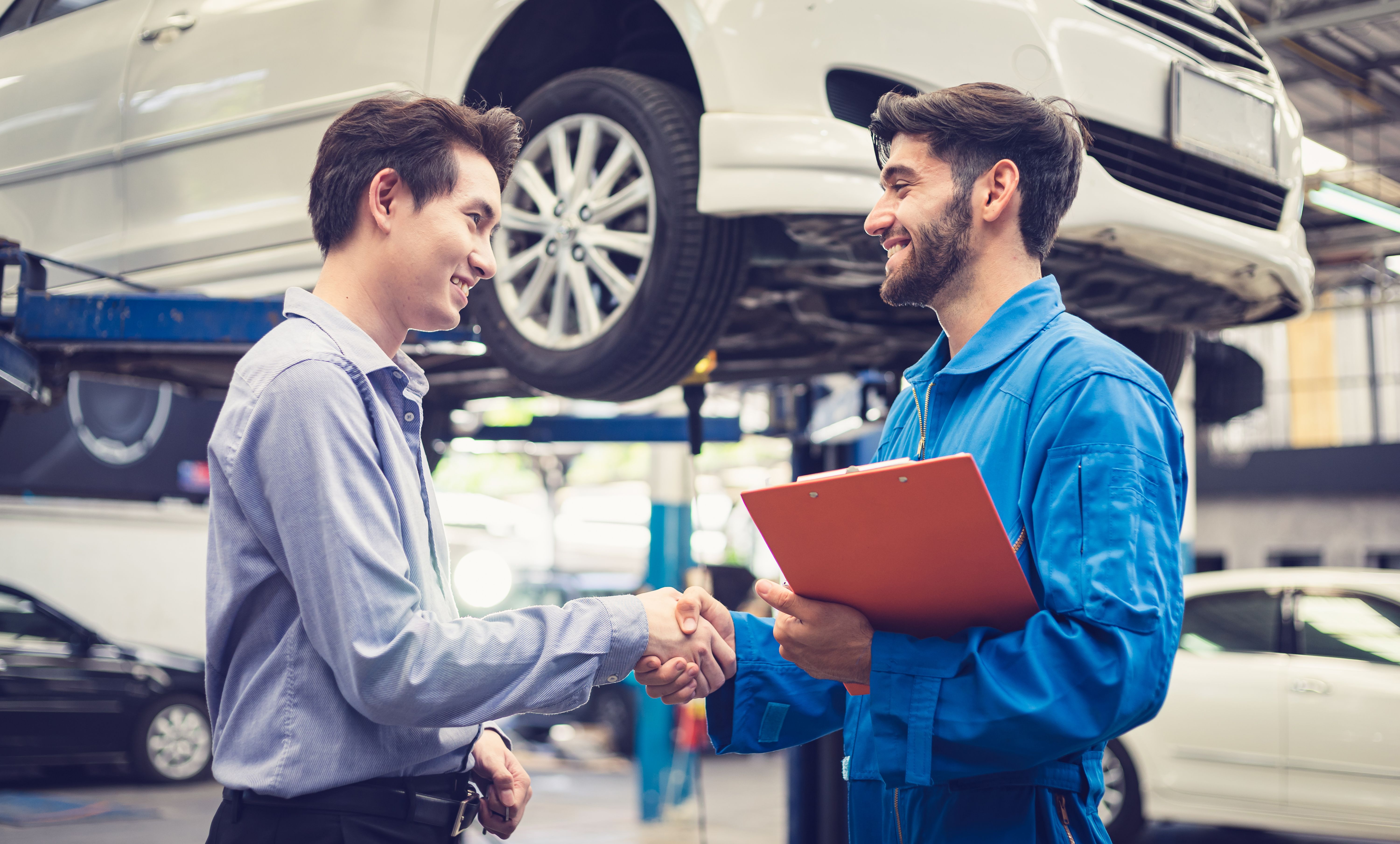 Mechanic holding clipboard shaking hands with car owner in the workshop garage. Car auto services concepts Mechanic holding clipboard shaking hands with car owner in the workshop garage. Car auto services concepts