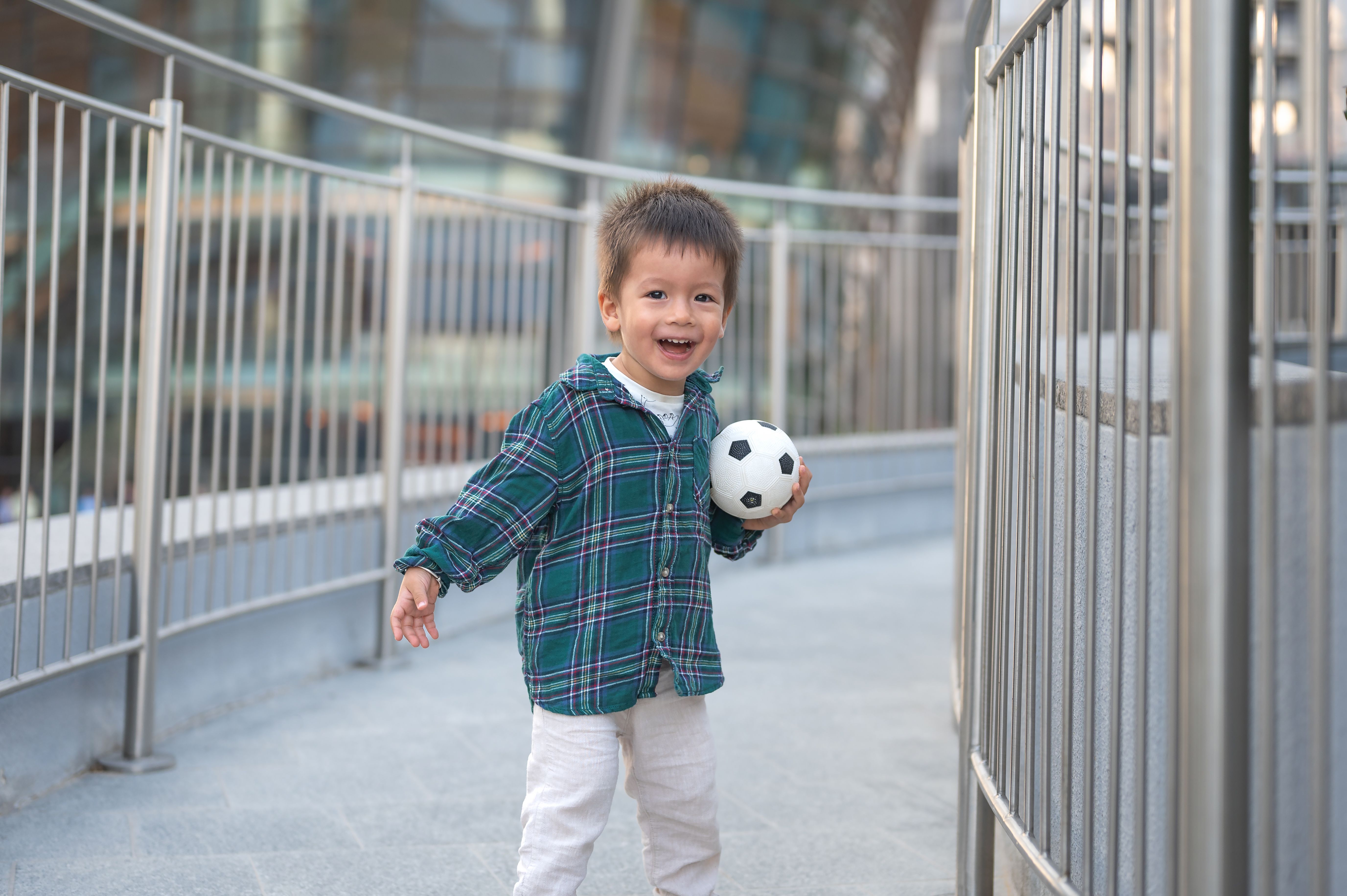 Toddler boy smiling holding soccer ball outdoor cityscape