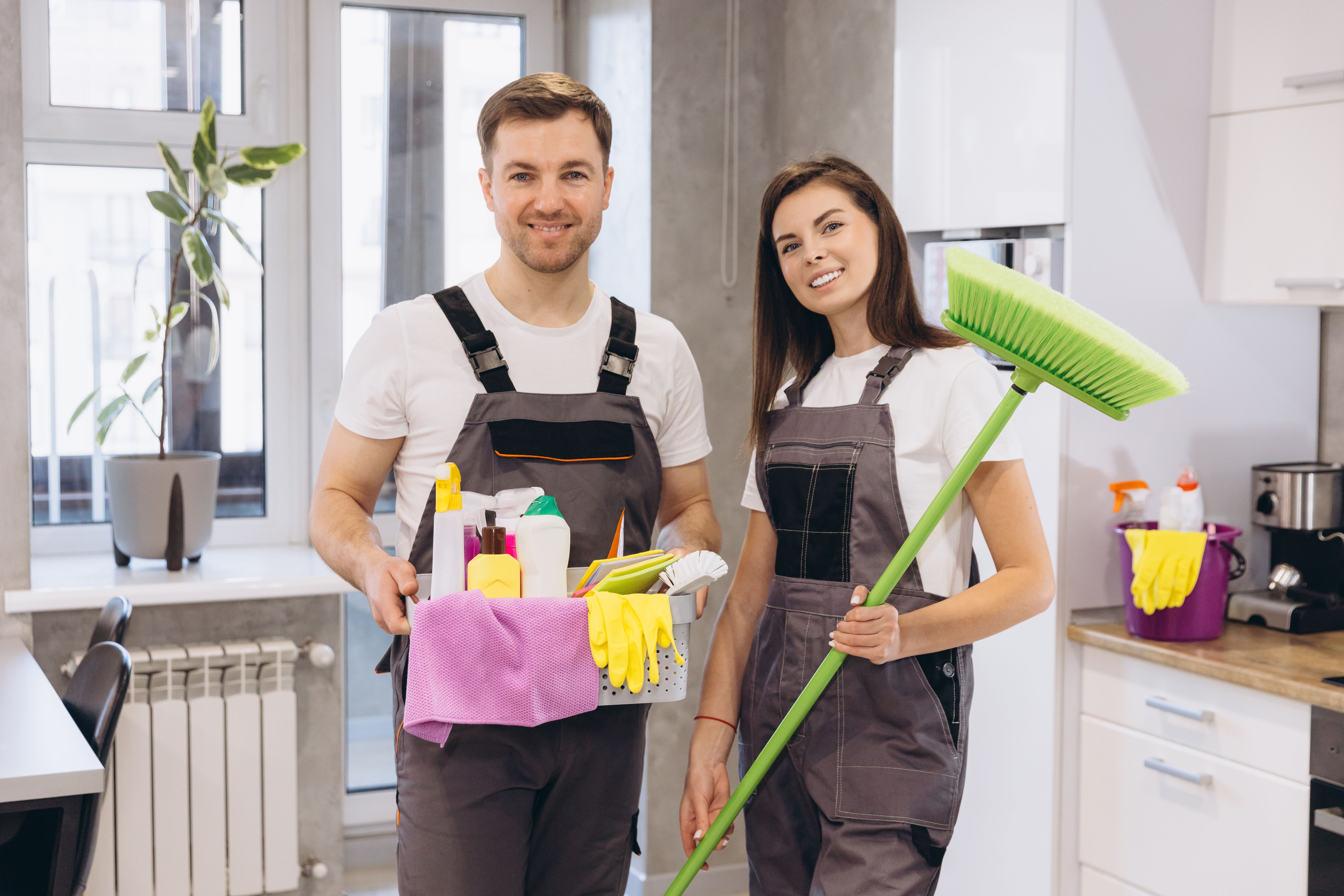 Cleaning company workers holding cleaning products and broom in kitchen