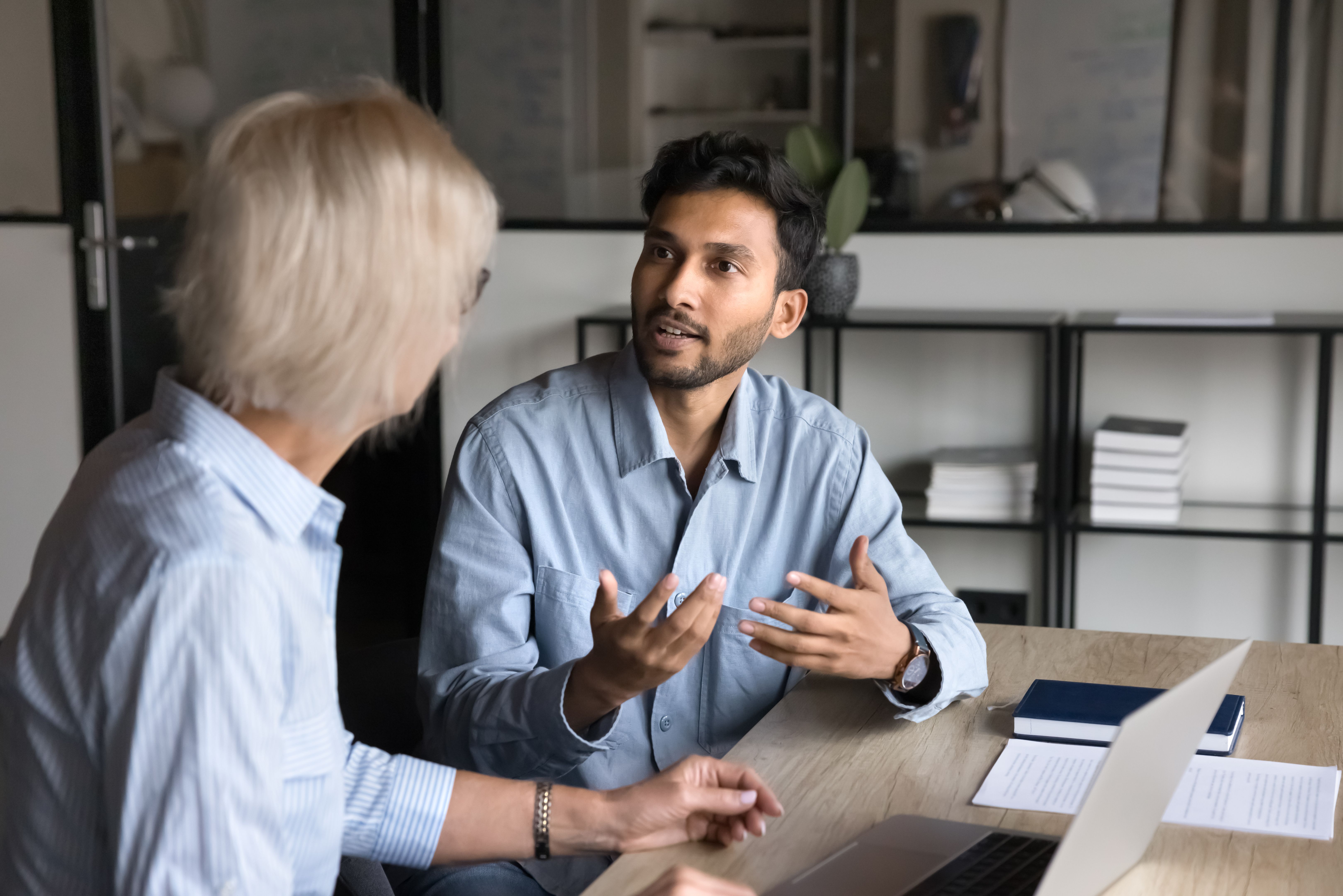Serious younger Indian professional man talking to elder colleague woman