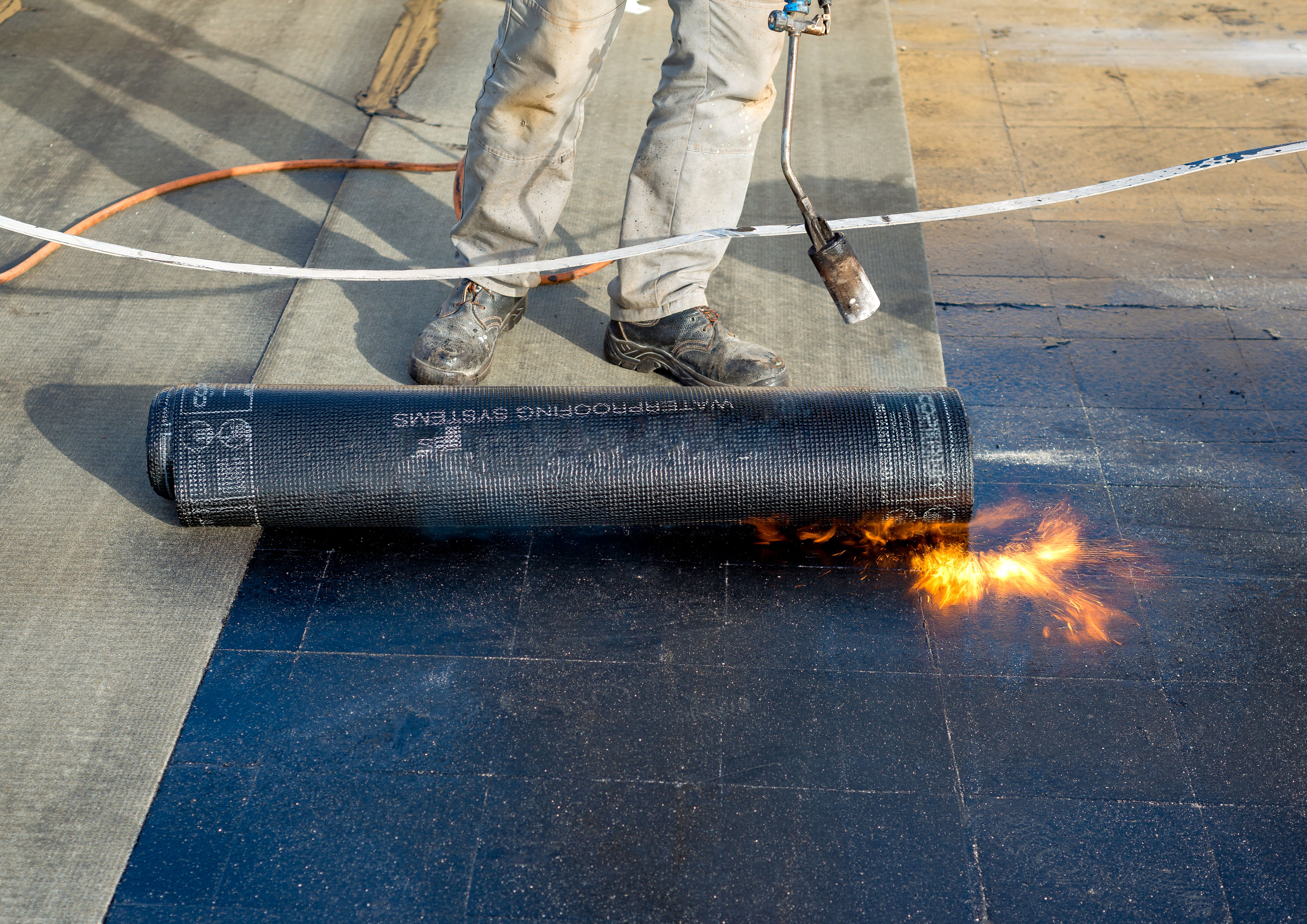 Worker preparing part of bitumen roofing felt roll for melting by gas heater torch flame. On the back of the sheath there is the stamp  