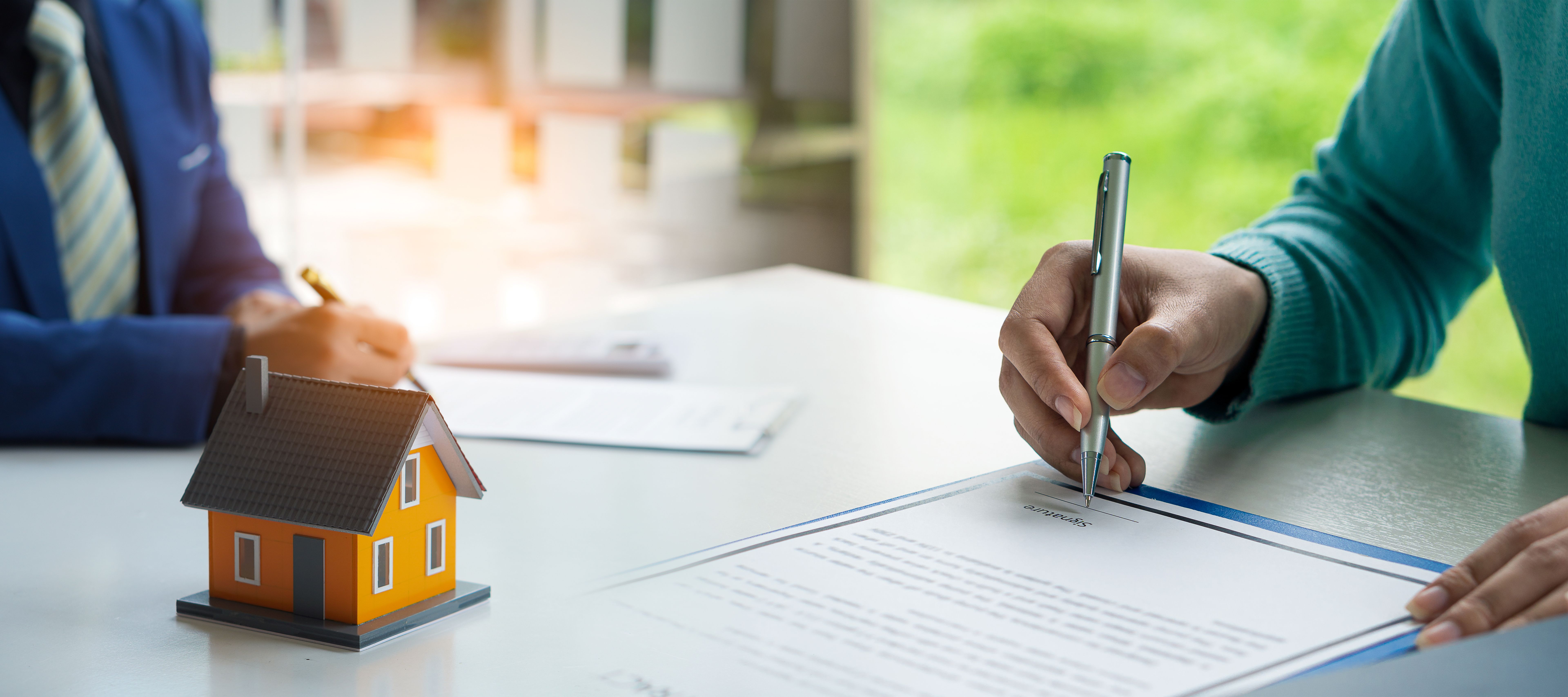 Real estate concept Young woman holding a pen signing a house purchase contract with a home sales representative in the office.