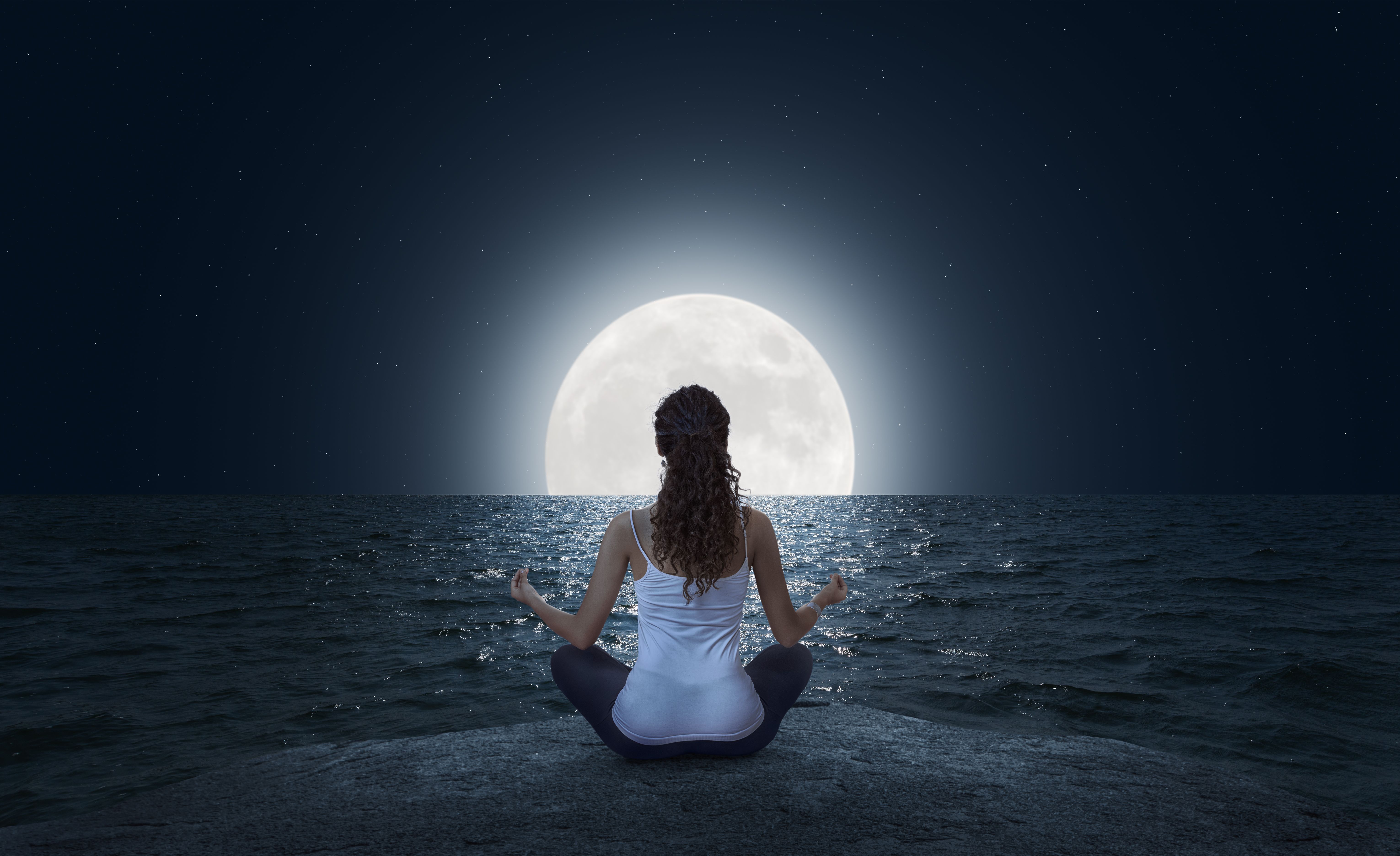 Young woman meditating on the beach at full moon