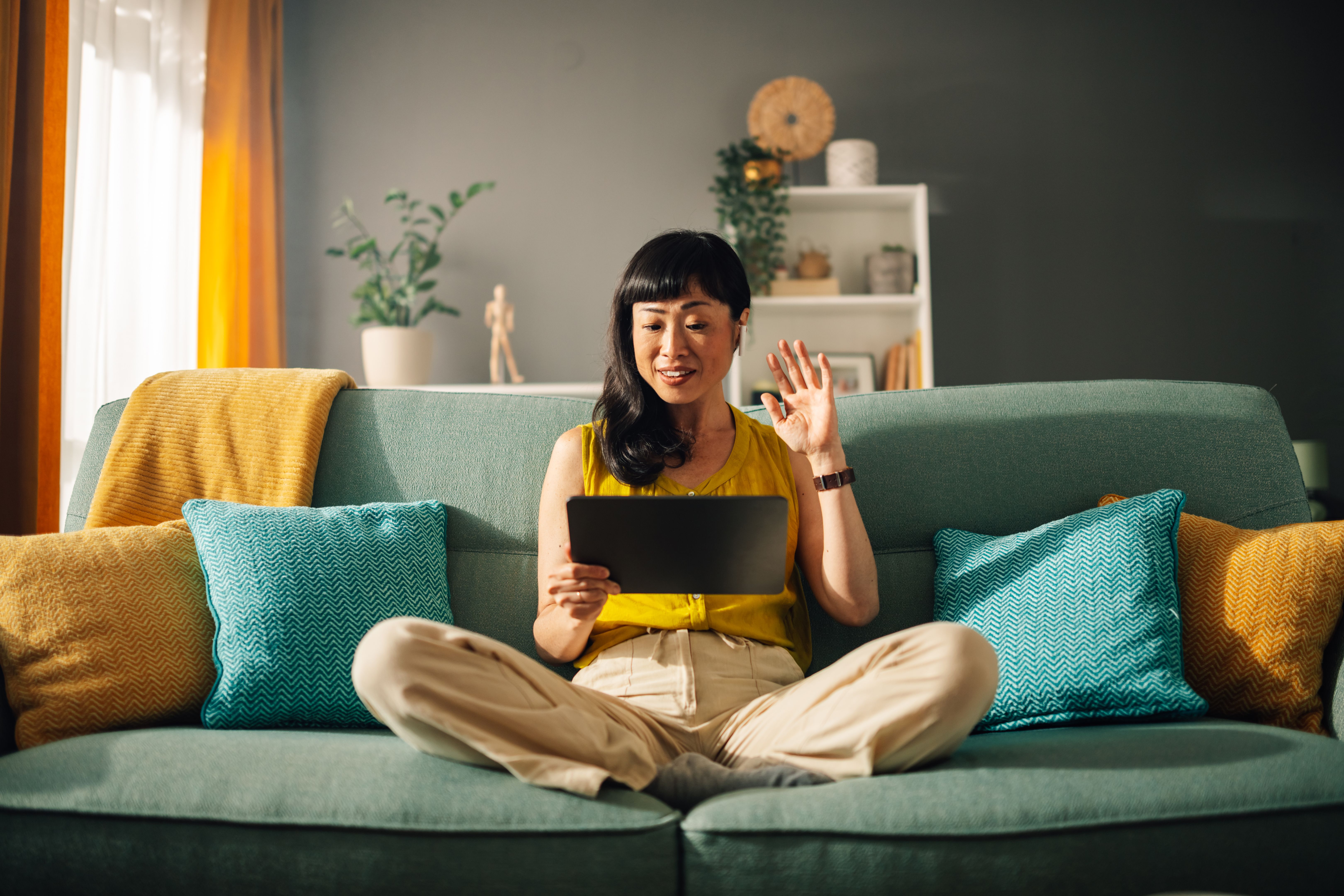 A young woman smiling and waving during a Grove session at Sage Collective on her couch.