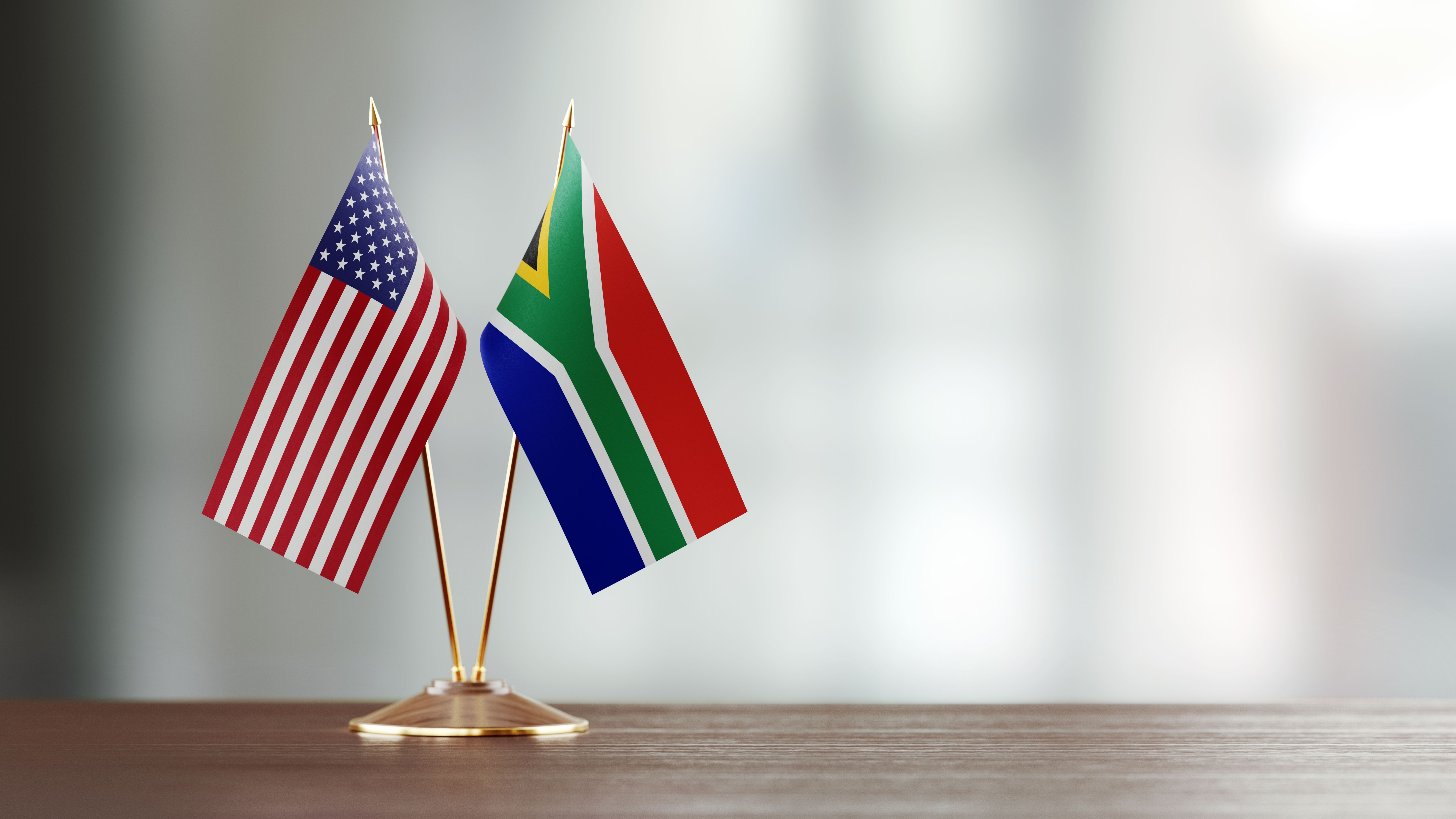 American And South African Flag Pair On A Desk Over Defocused Background