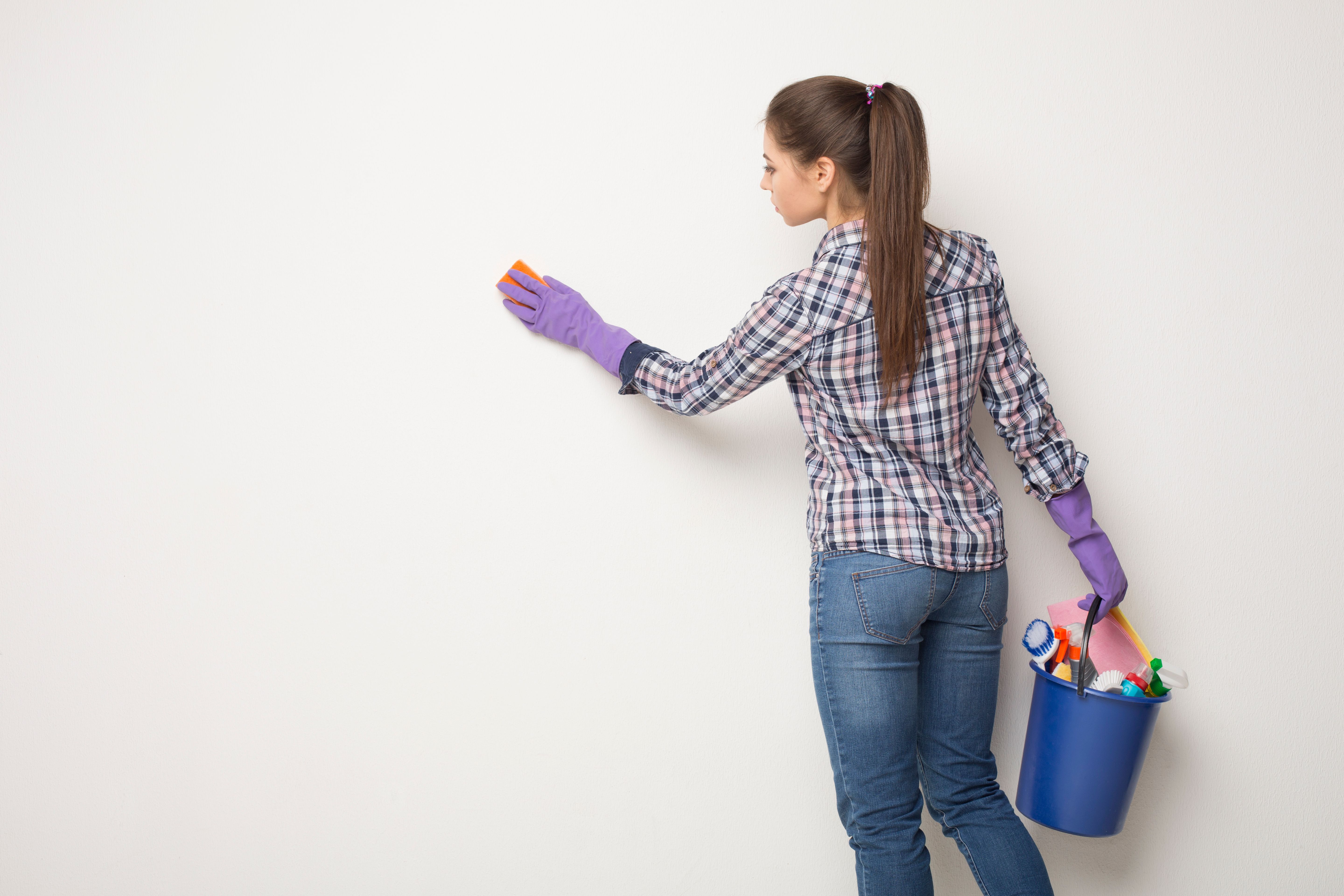 Young woman wiping white wall from dust