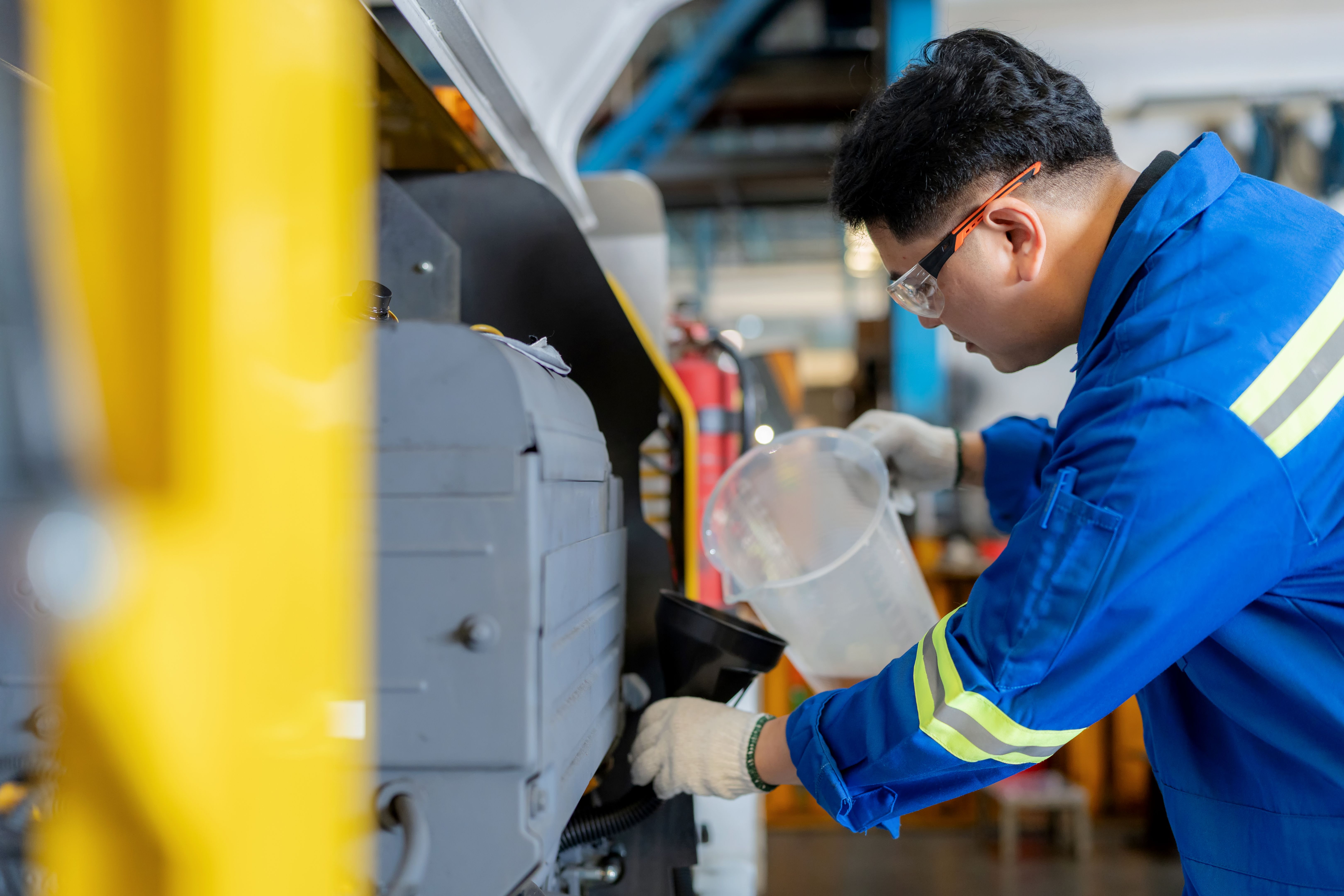 Engineer in uniform wearing gloves refills motor oil through filter funnel into cargo loader engine. Concept of industrial maintenance, lubrication, and safety operation in airport freight transportation and repair service.