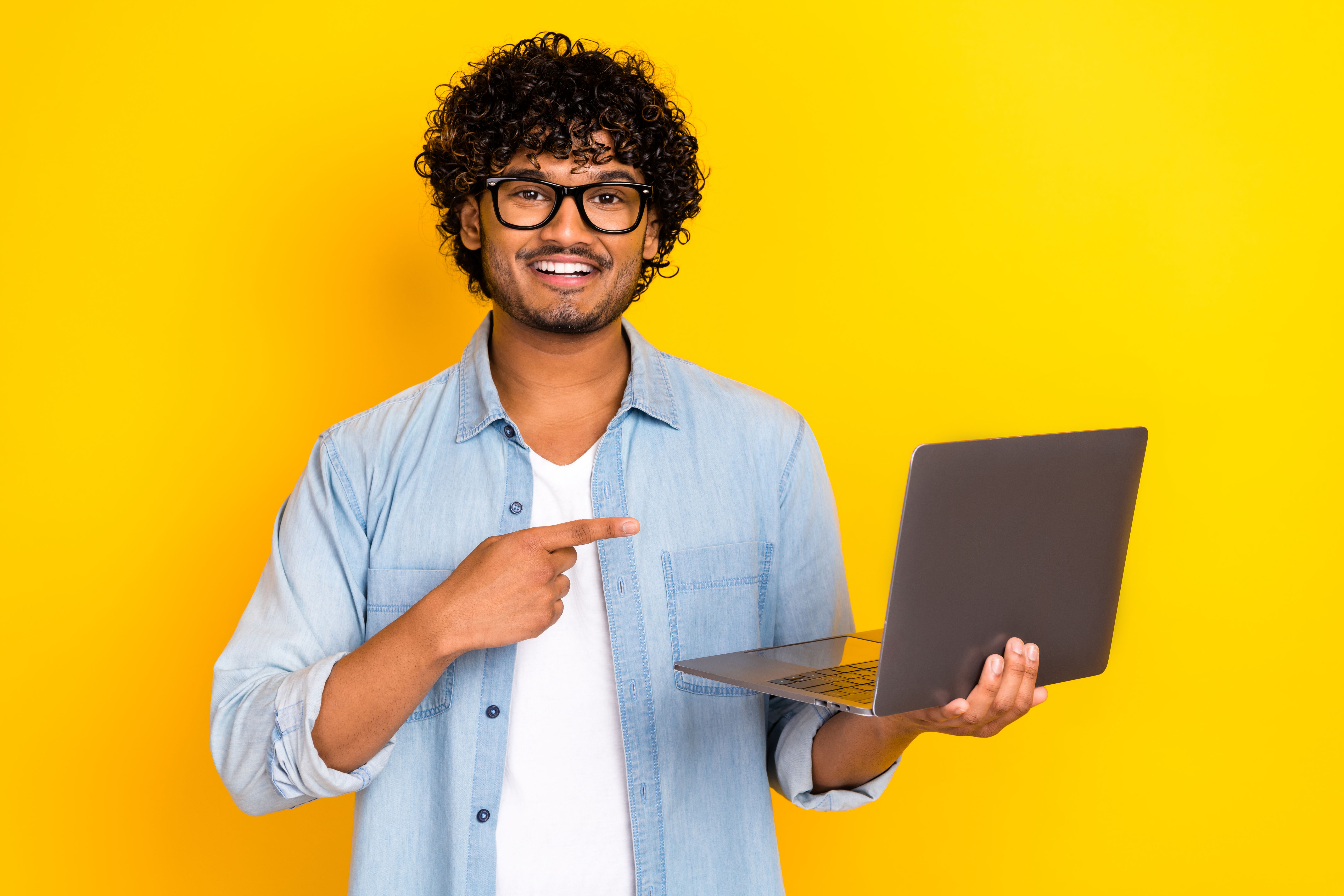 Foto de um cara bonito e alegre indica o netbook microsoft da maçã do dedo isolado no fundo de cor amarela