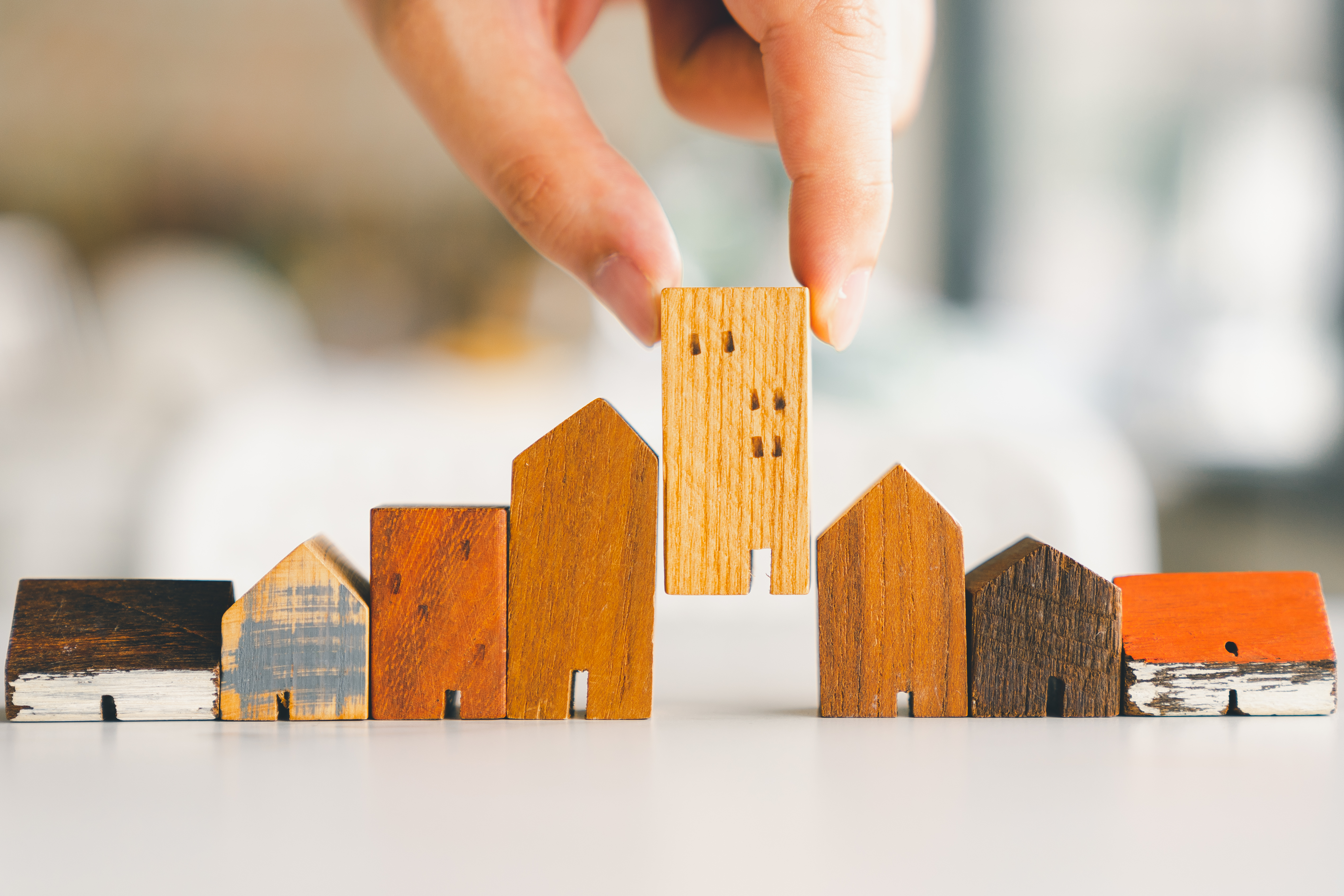 Hand choosing mini wood house model from model and row of coin money on wood table, selective focus, Planning to buy property. Choose what's the best. A symbol for construction ,ecology, loan concepts Hand choosing mini wood house model from model and row of coin money on wood table, selective focus, Planning to buy property. Choose what's the best. A symbol for construction ,ecology, loan concepts