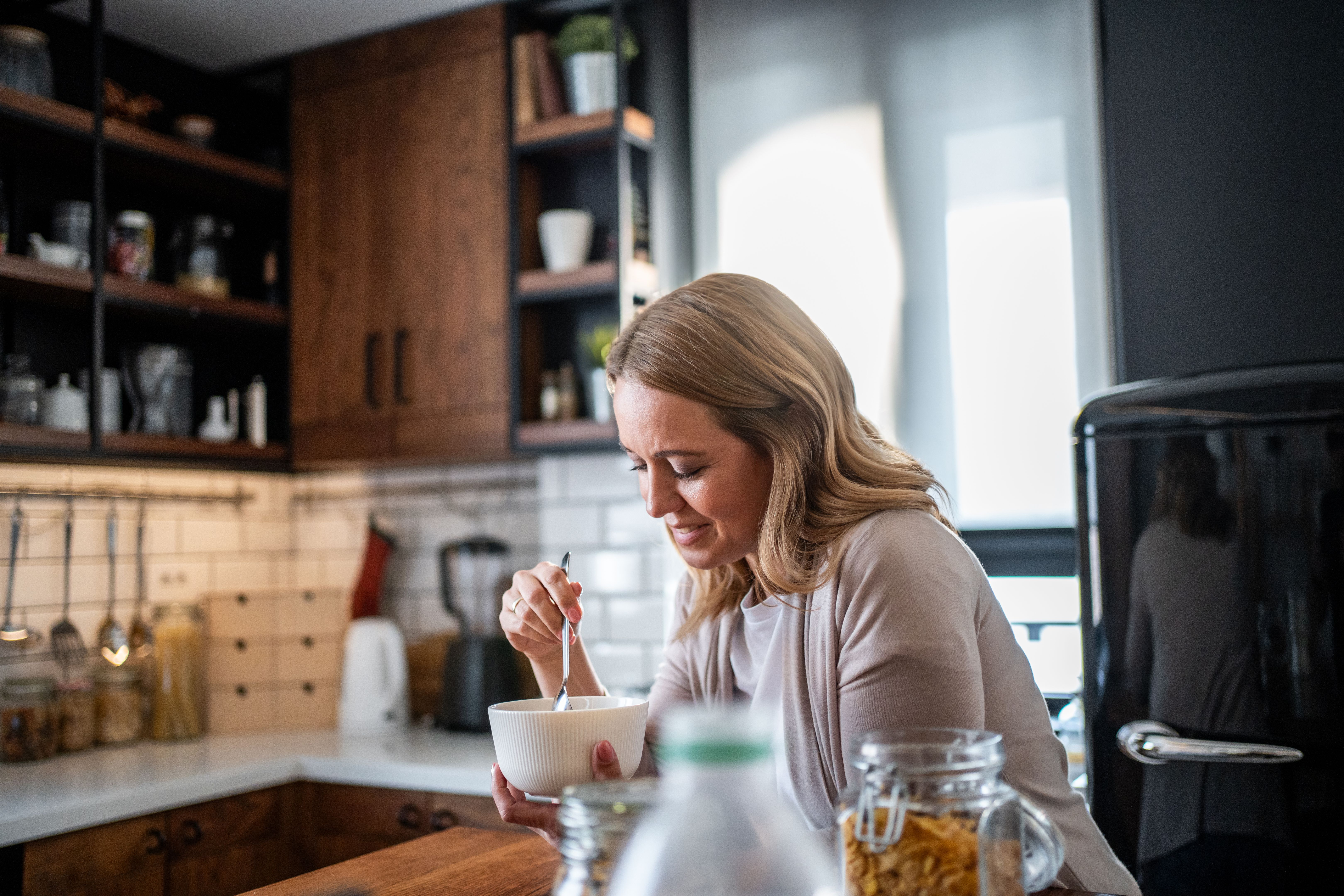 Woman feeling sad while eating breakfast cereal in kitchen Woman feeling sad while eating breakfast cereal in kitchen