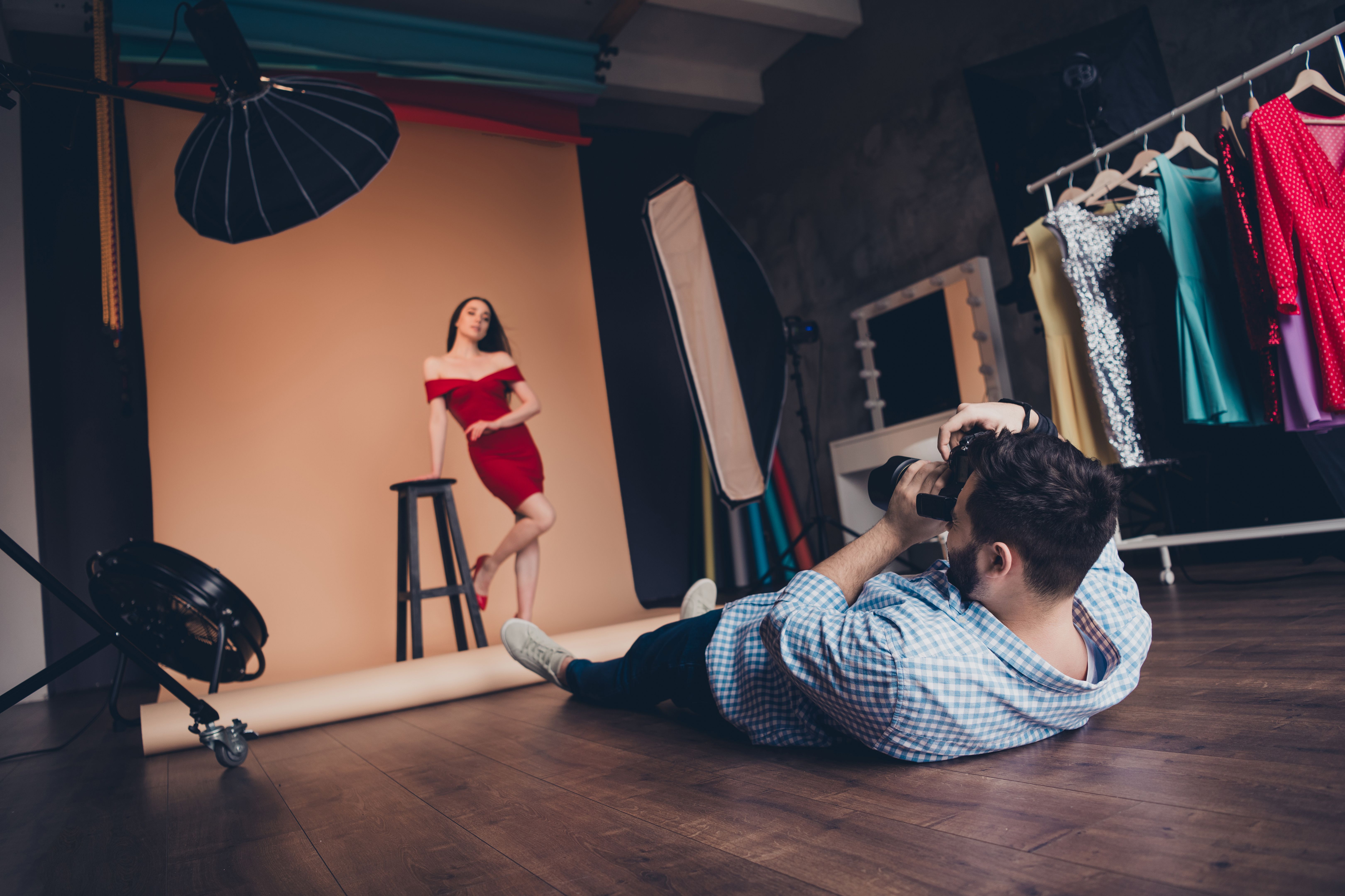 Fashion photographer lying and taking photo of beautiful female model posing in modern art studio indoors