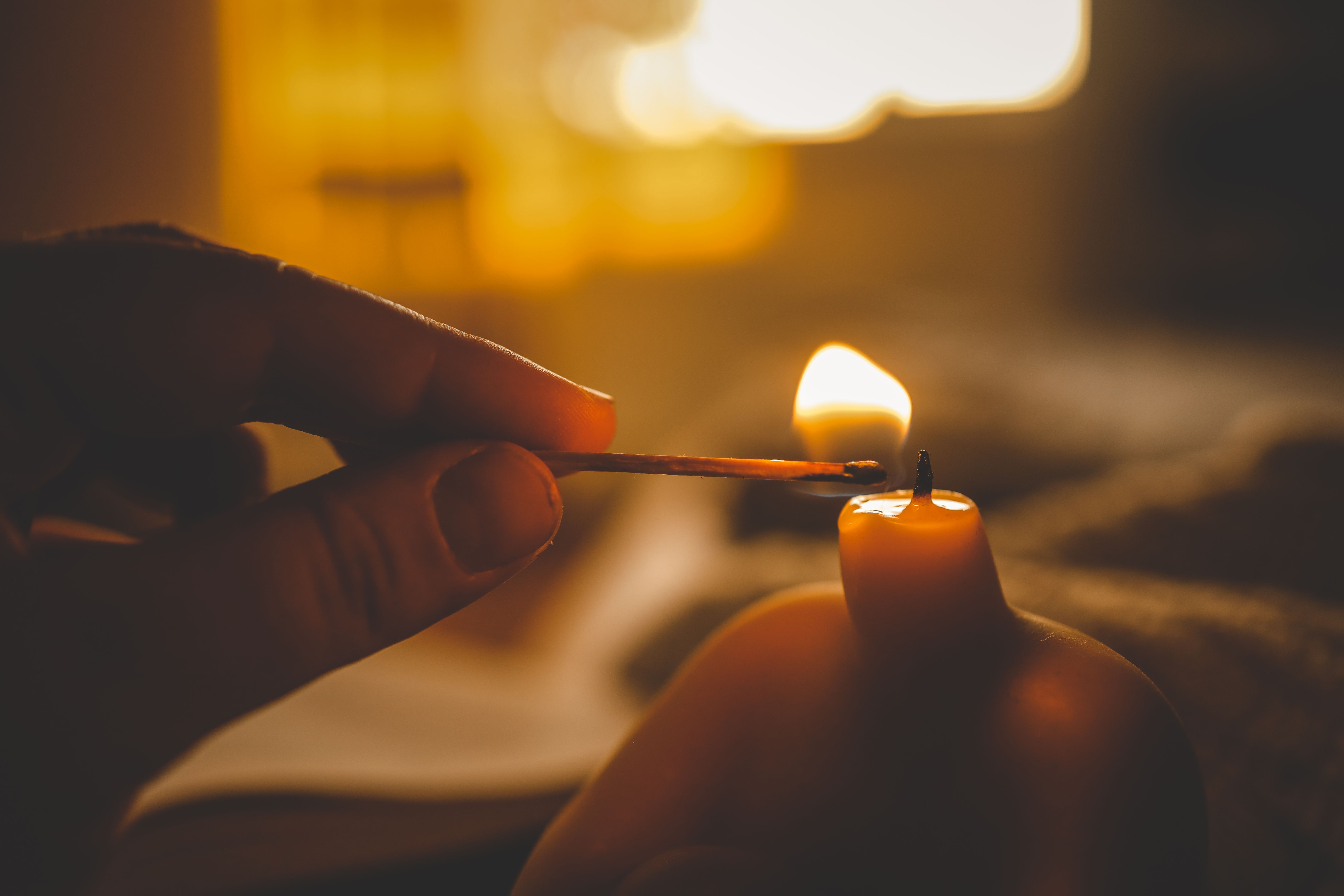 Close-up of a hand lighting a sculptural candle with a match in warm ambient light