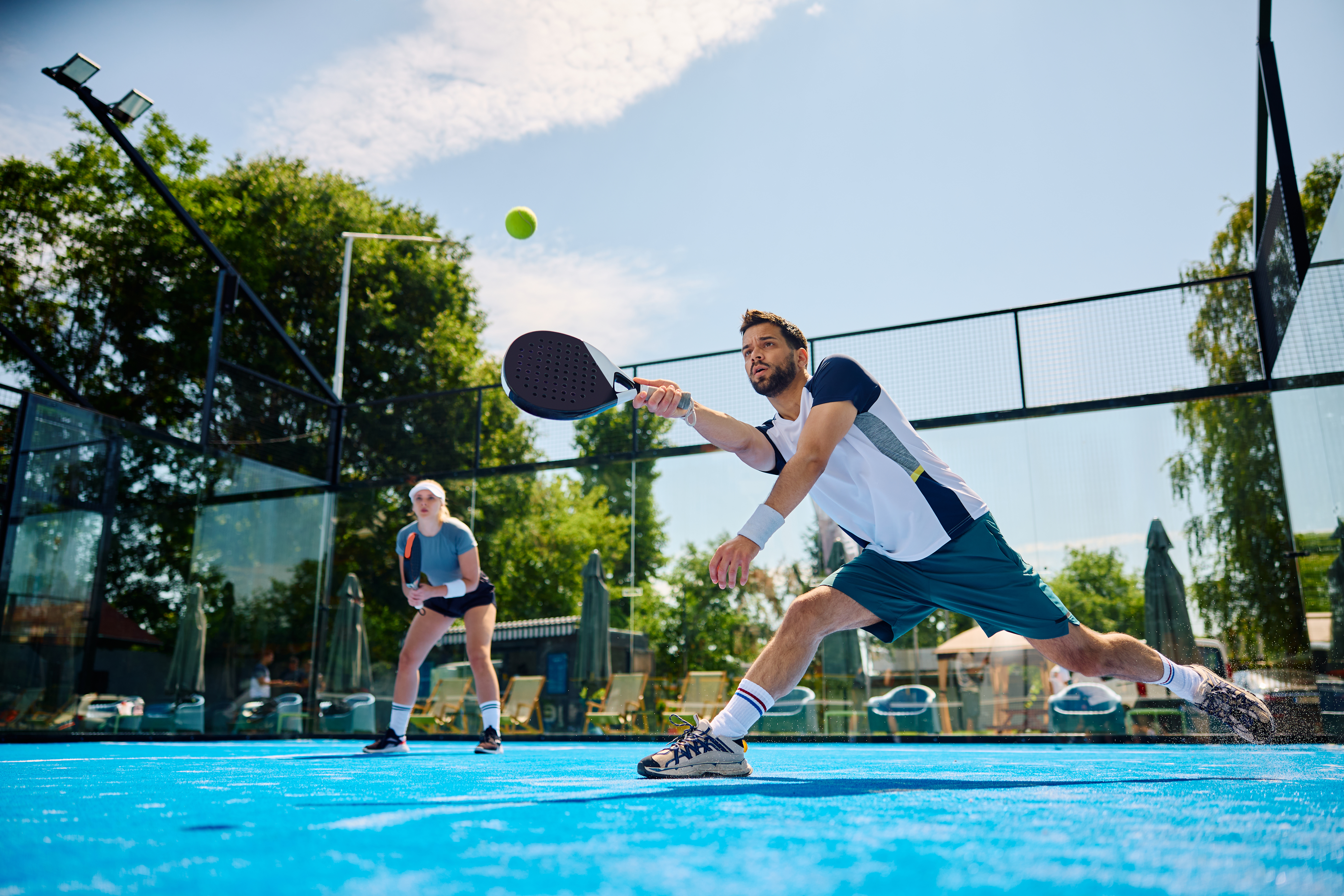Joueur de paddle-tennis faisant un effort pour frapper la balle pendant un match sur un court extérieur. Joueur de paddle-tennis faisant un effort pour frapper la balle pendant un match sur un court extérieur.