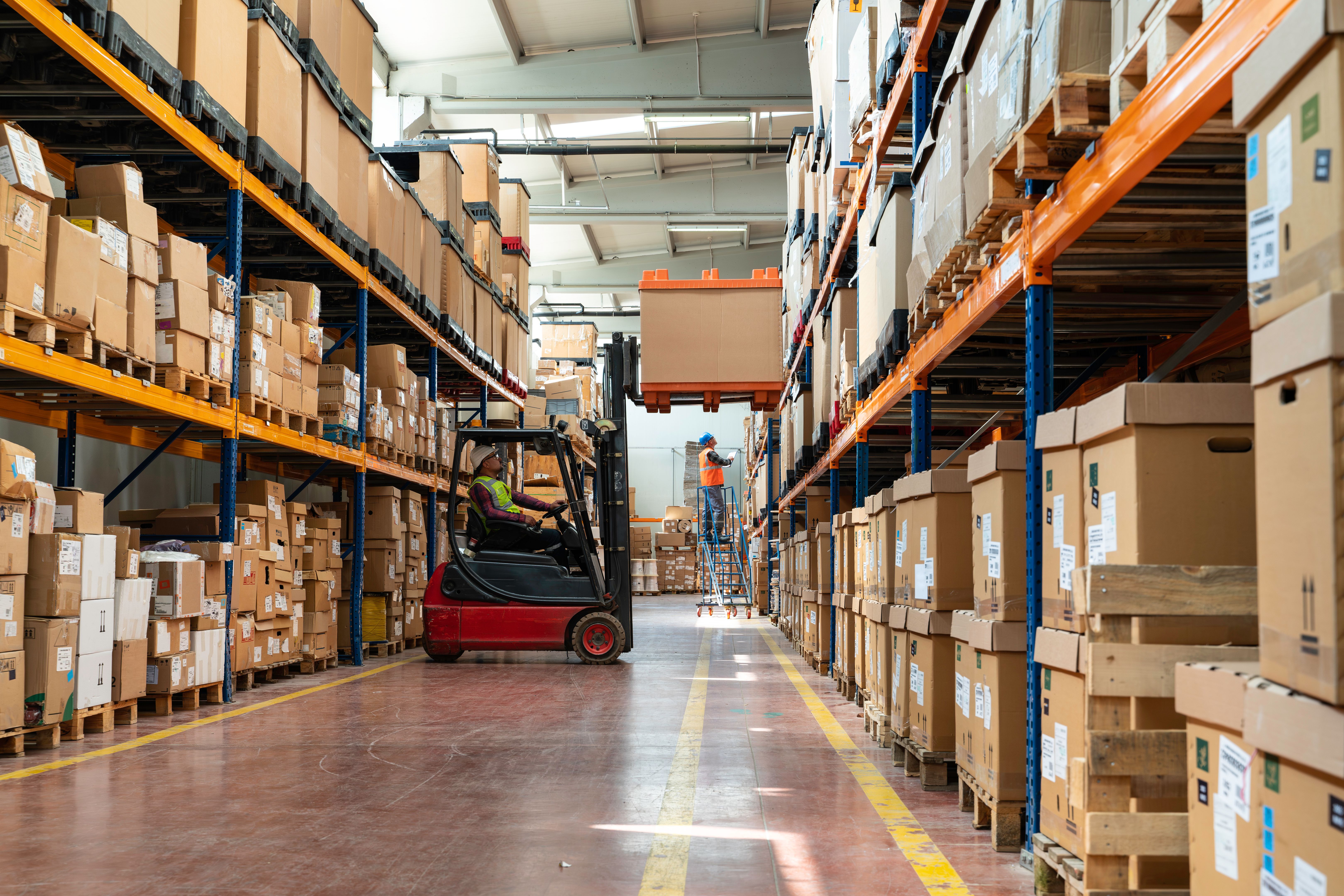 Uniformed Worker Driving and Loading Cardboard Boxes with Forklift Stacker Loader in a Factory Warehouse