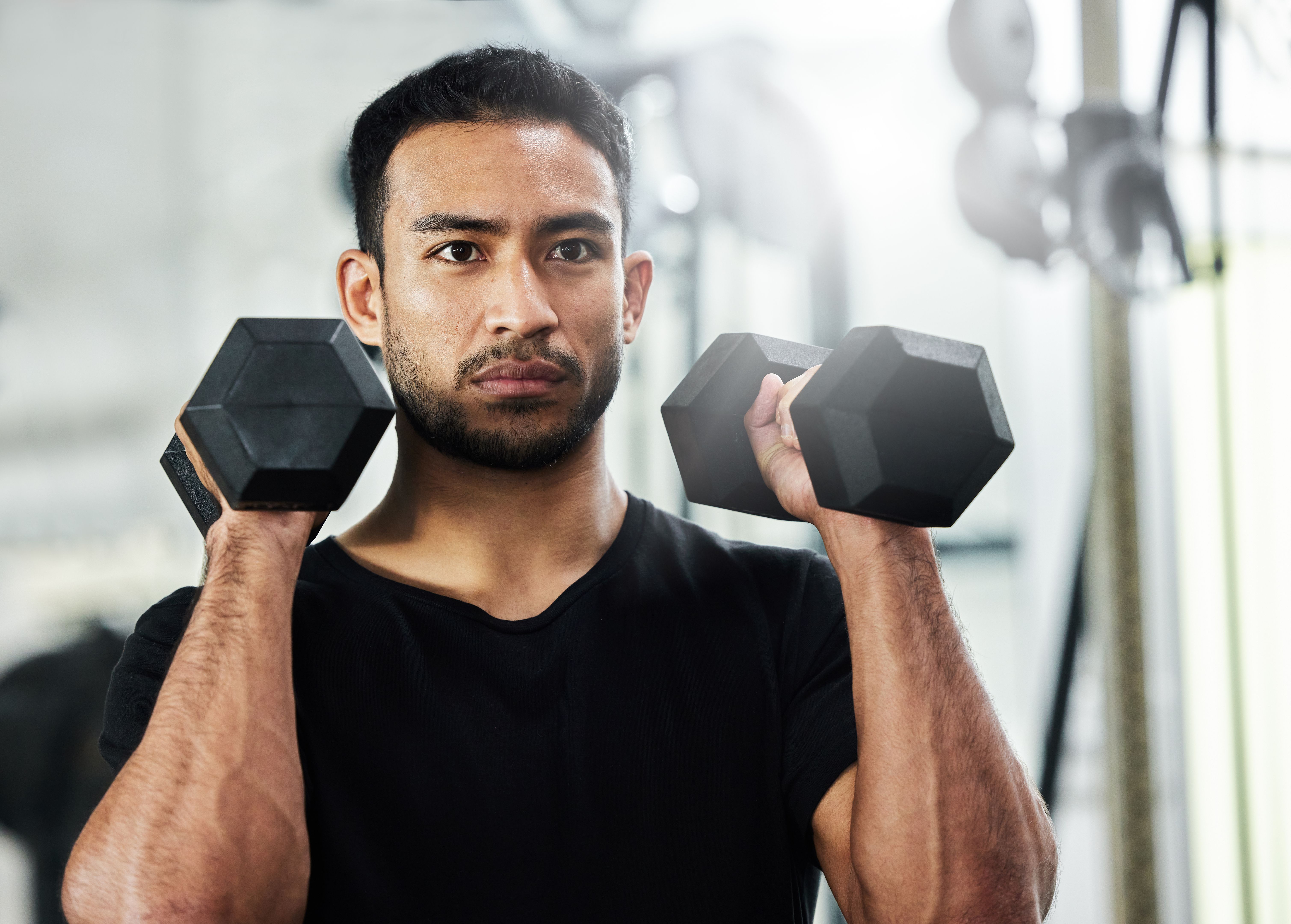 Shot of a handsome young man working out with dumbbells at the gym