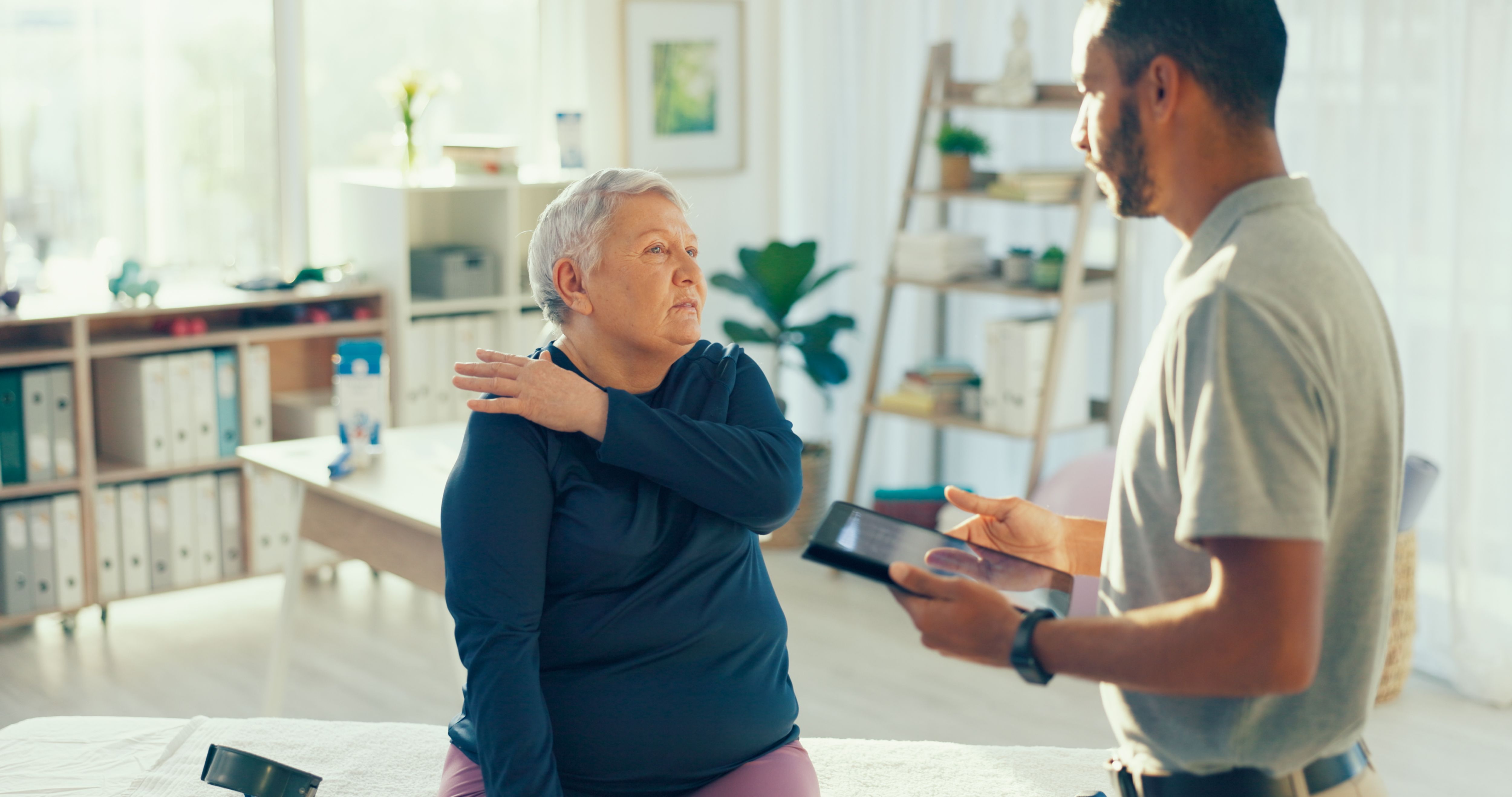 Shoulder pain, tablet and physiotherapist with mature woman for service, consulting and wellness. Healthcare, chiropractor and patient on digital tech for physical therapy, recovery and online report Shoulder pain, tablet and physiotherapist with mature woman for service, consulting and wellness. Healthcare, chiropractor and patient on digital tech for physical therapy, recovery and online report