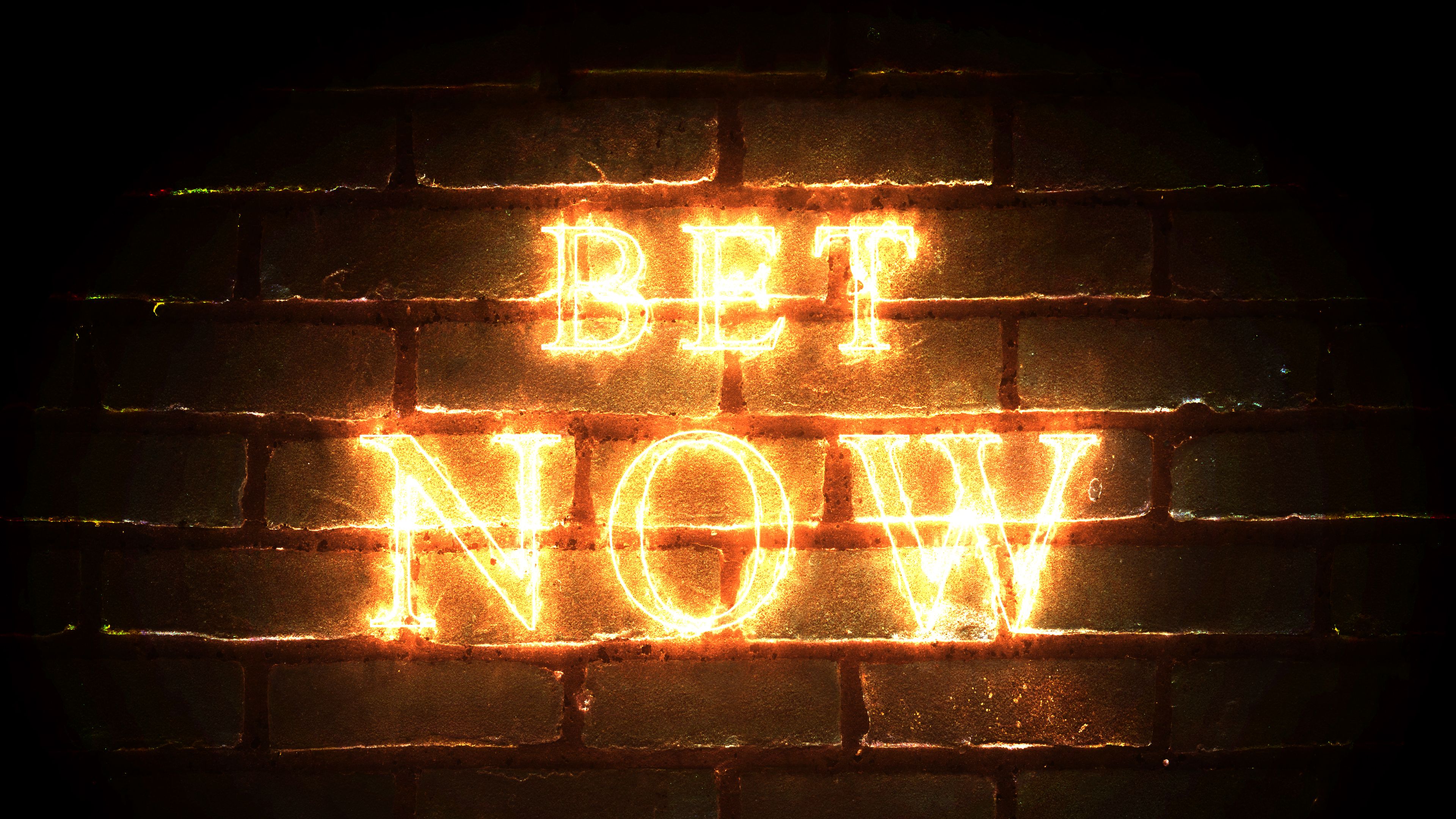 Bet Now glowing fiery inscription on brick wall background. Bet Now glowing fiery inscription on brick wall background.