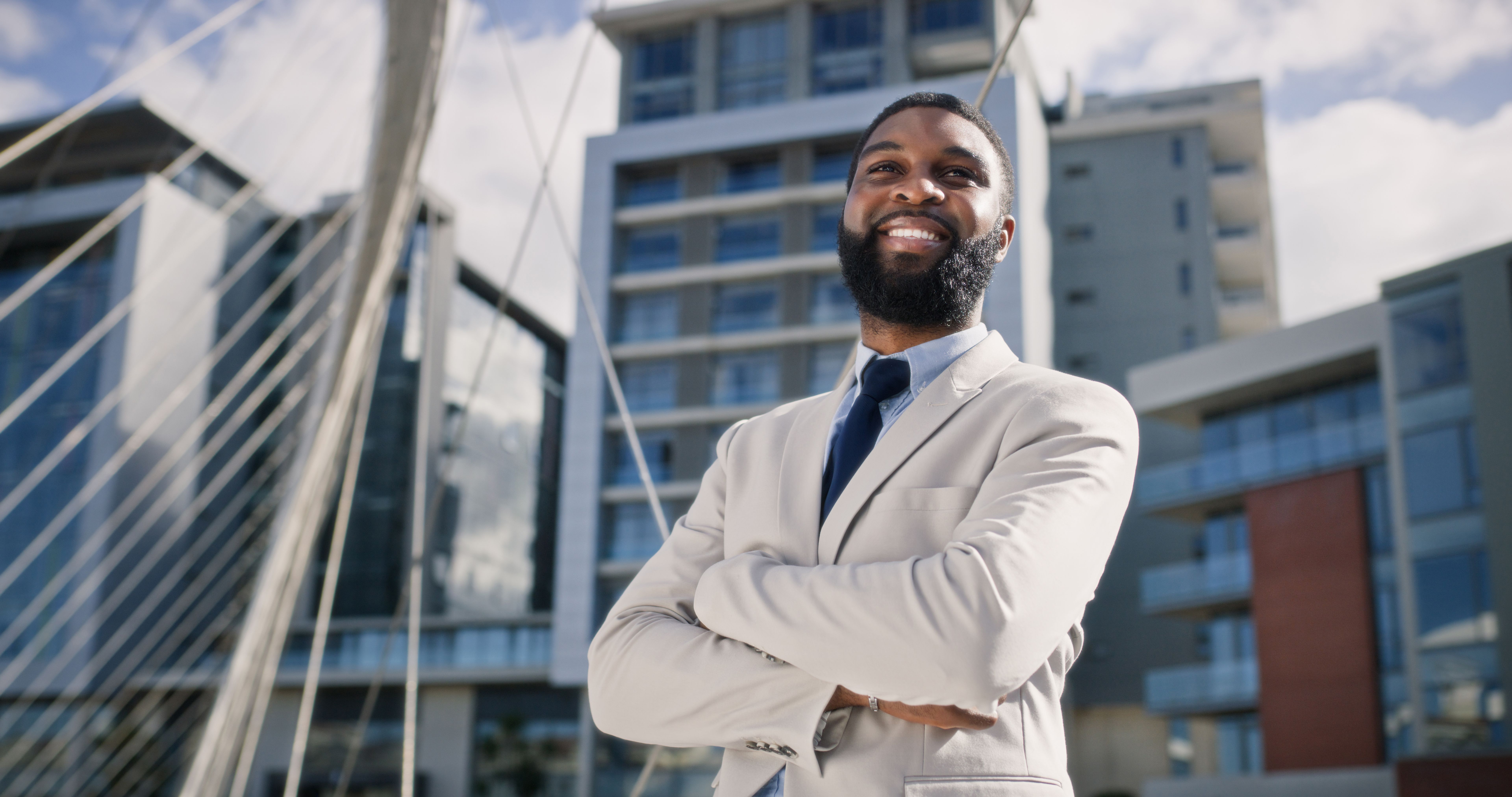 Businessman, smile and city confidence with arms crossed as professional entrepreneur, opportunity or future. Black person, building and bridge in New York as finance consultant, travel or commute