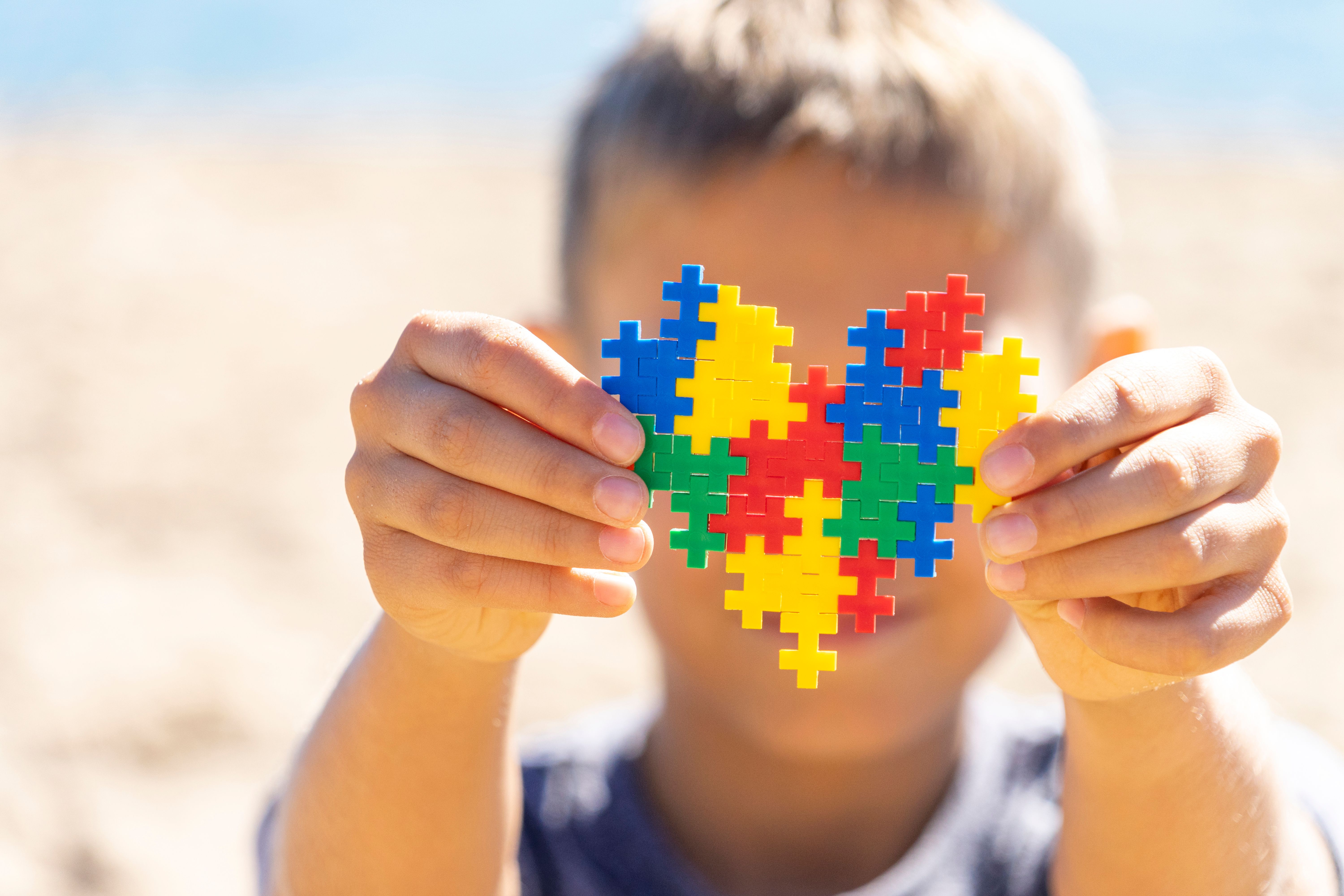 Boy holding colorful puzzle heart in front of his face. World autism awareness day concept Boy holding colorful puzzle heart in front of his face. World autism awareness day concept