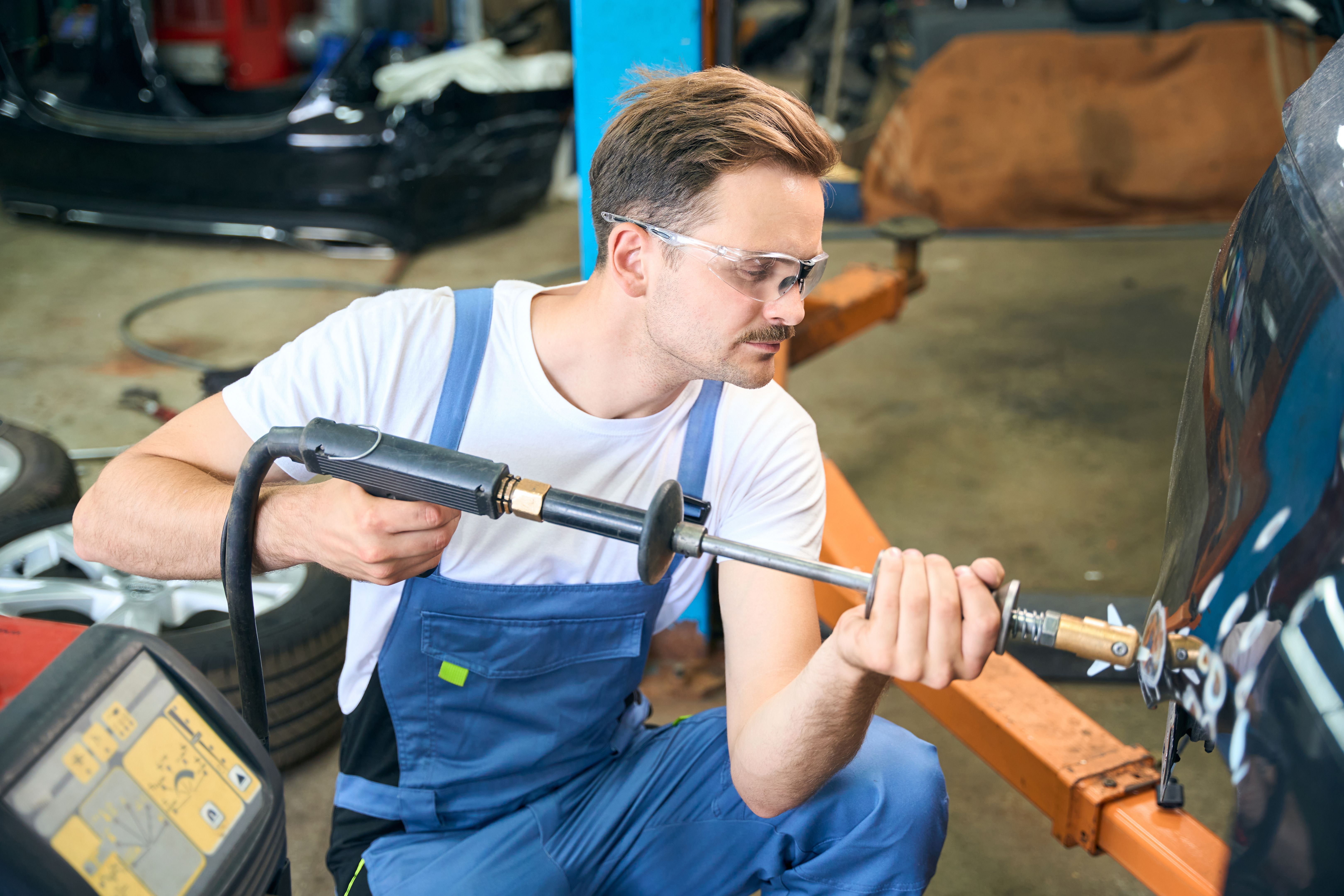 Male worker in protective glasses using spotter in the hands during repair work Male worker in protective glasses using spotter in the hands during repair work