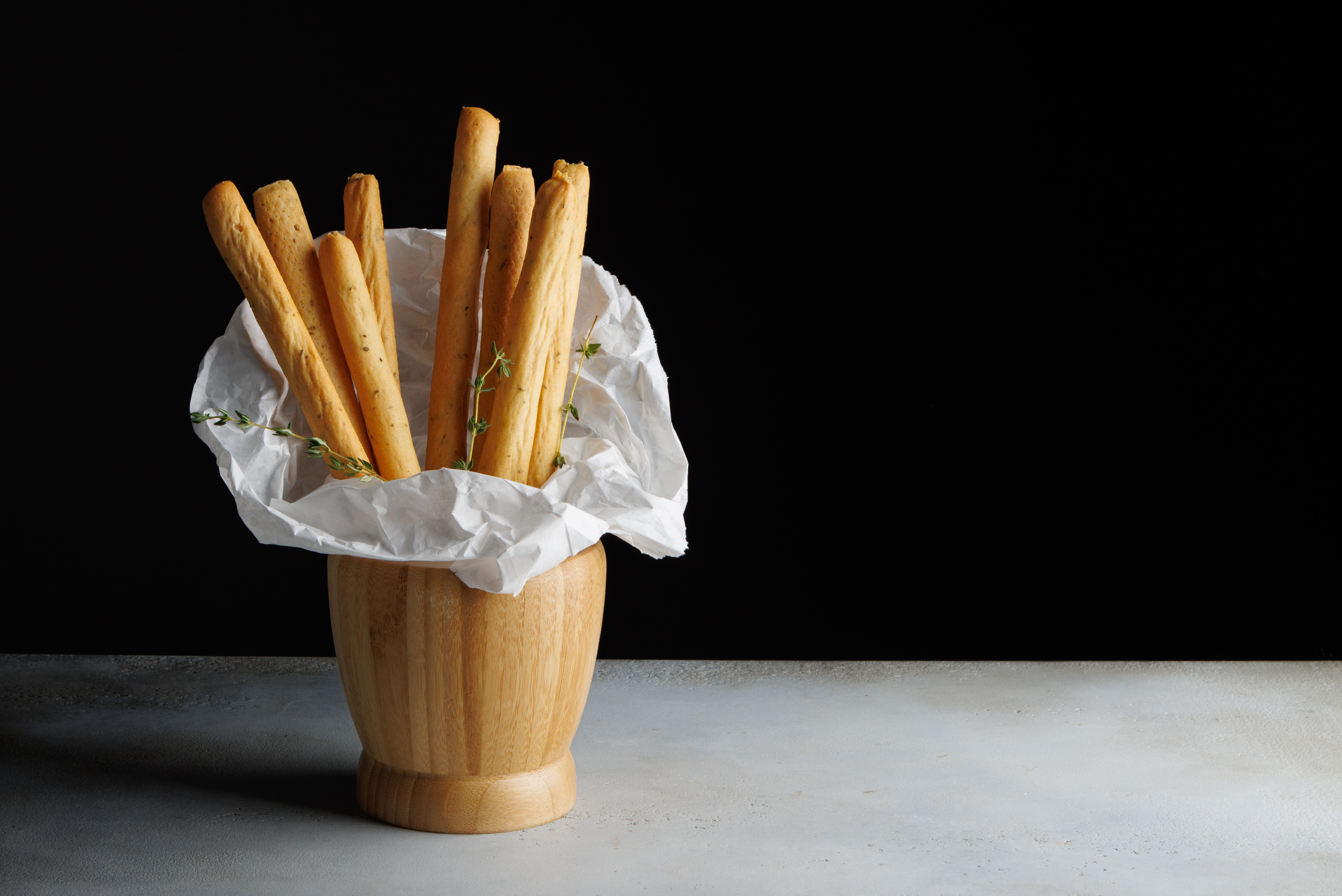 Grissini in Wooden Vase on Concrete Table with Craft Paper and Dark Background