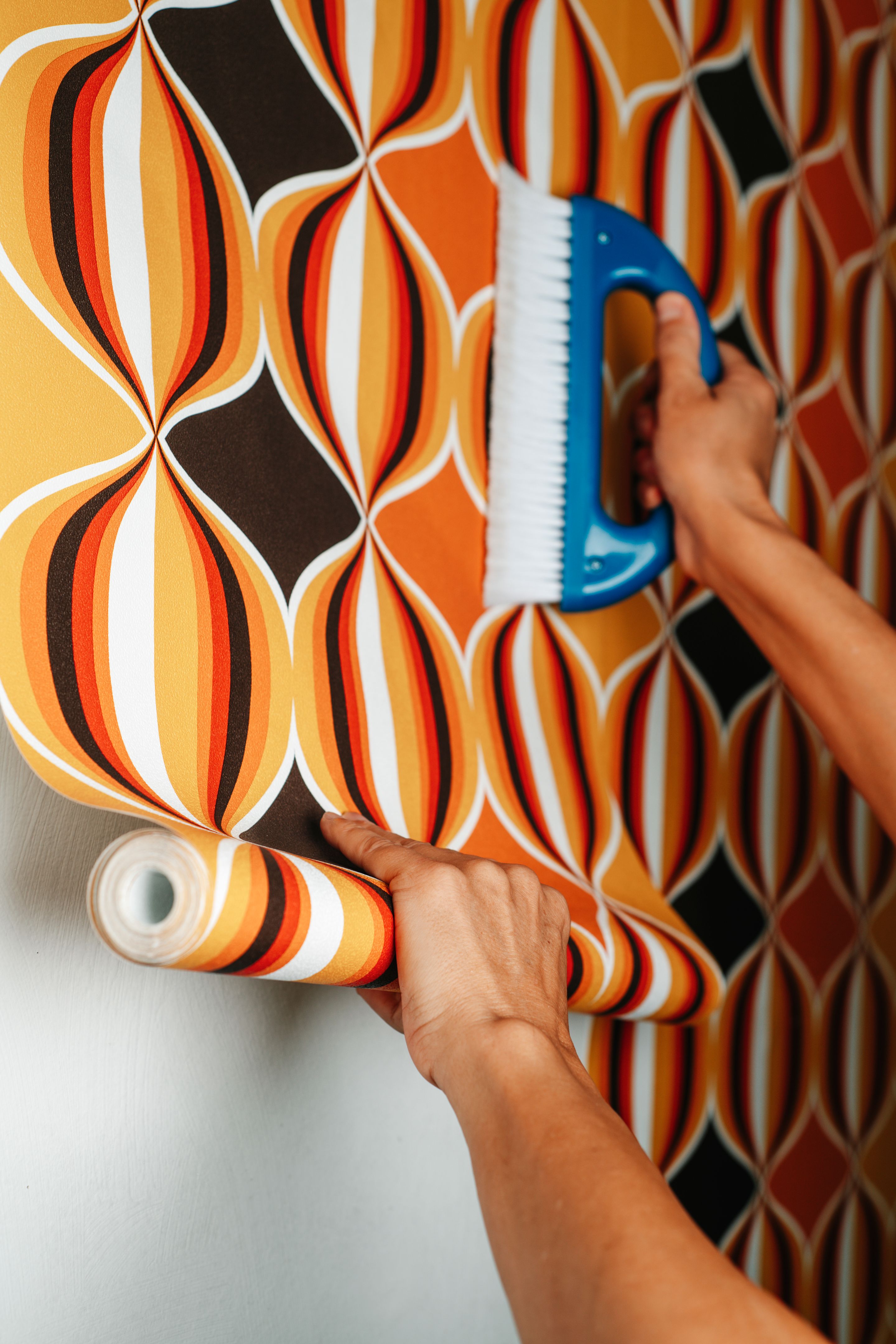 uses a blue brush to attach wallpaper to a wall