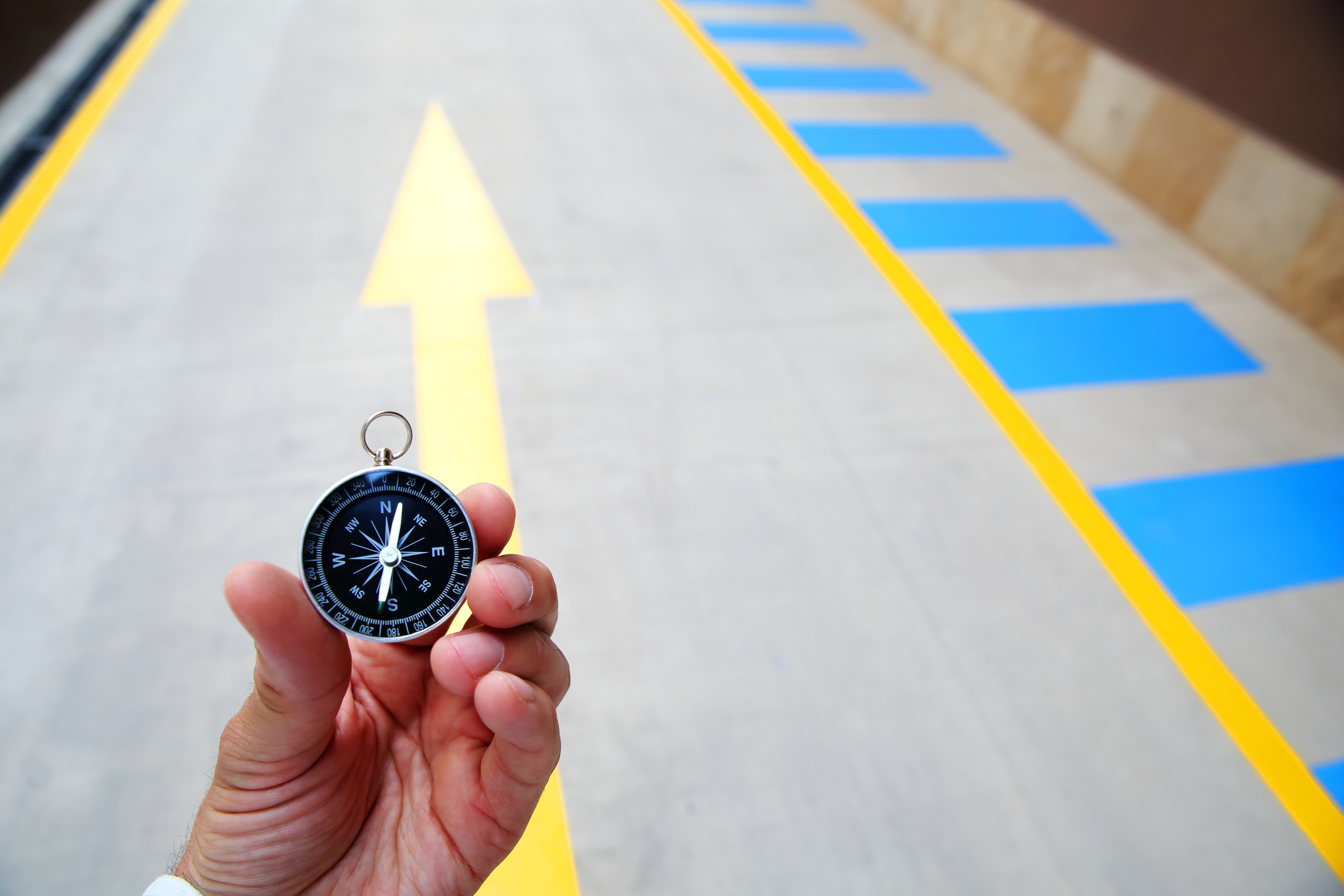 Hand holding a compass with a large arrow painted on the ground, symbolizing strategic alignment and direction toward organisational goals.
