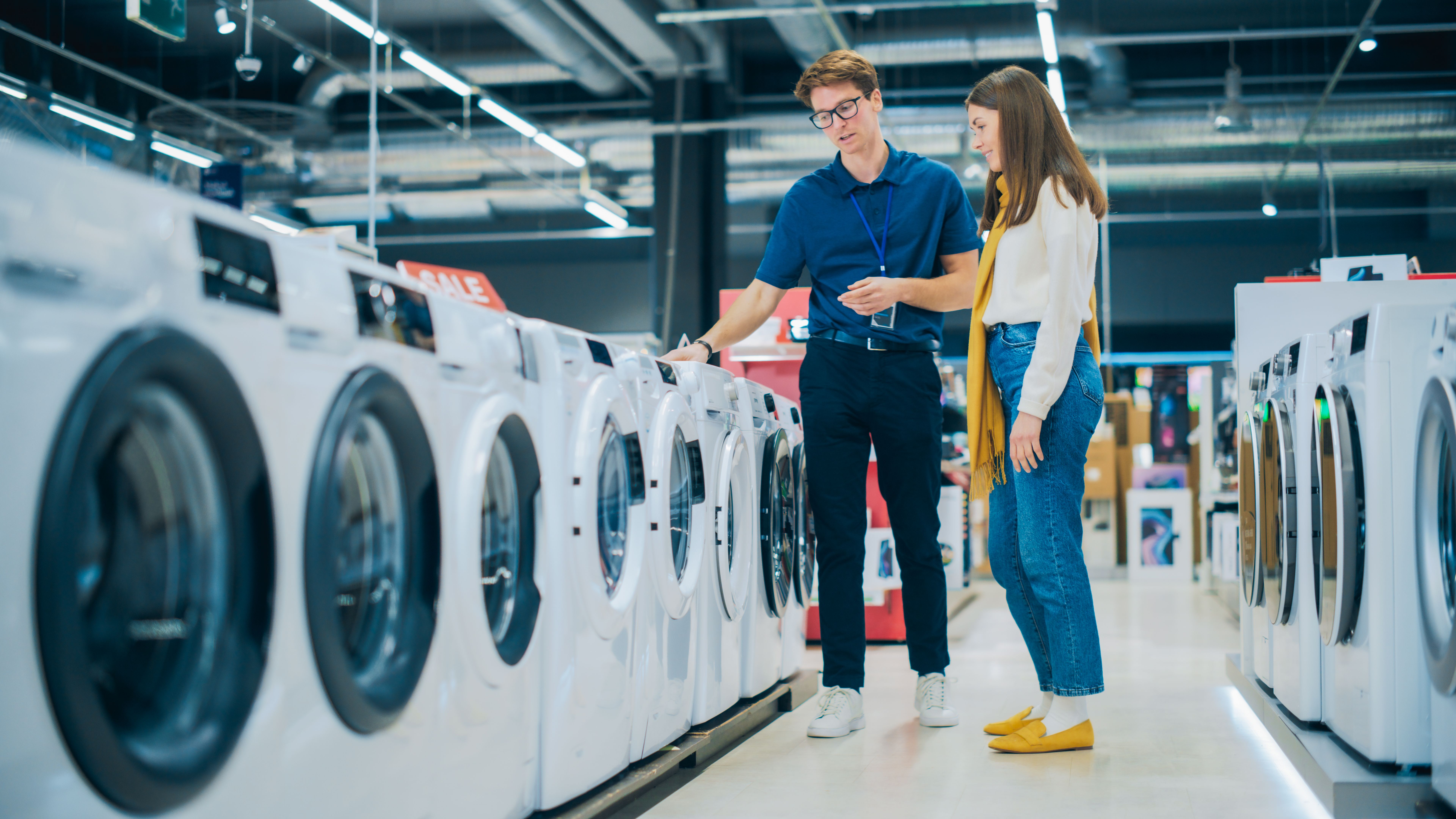Portrait of a Female Customer Seeking Expert Advice from Retail Home Electronics Expert for Washing Machine Purchase. Young Woman Explores Contemporary Laundry Appliance Options in a Department Store