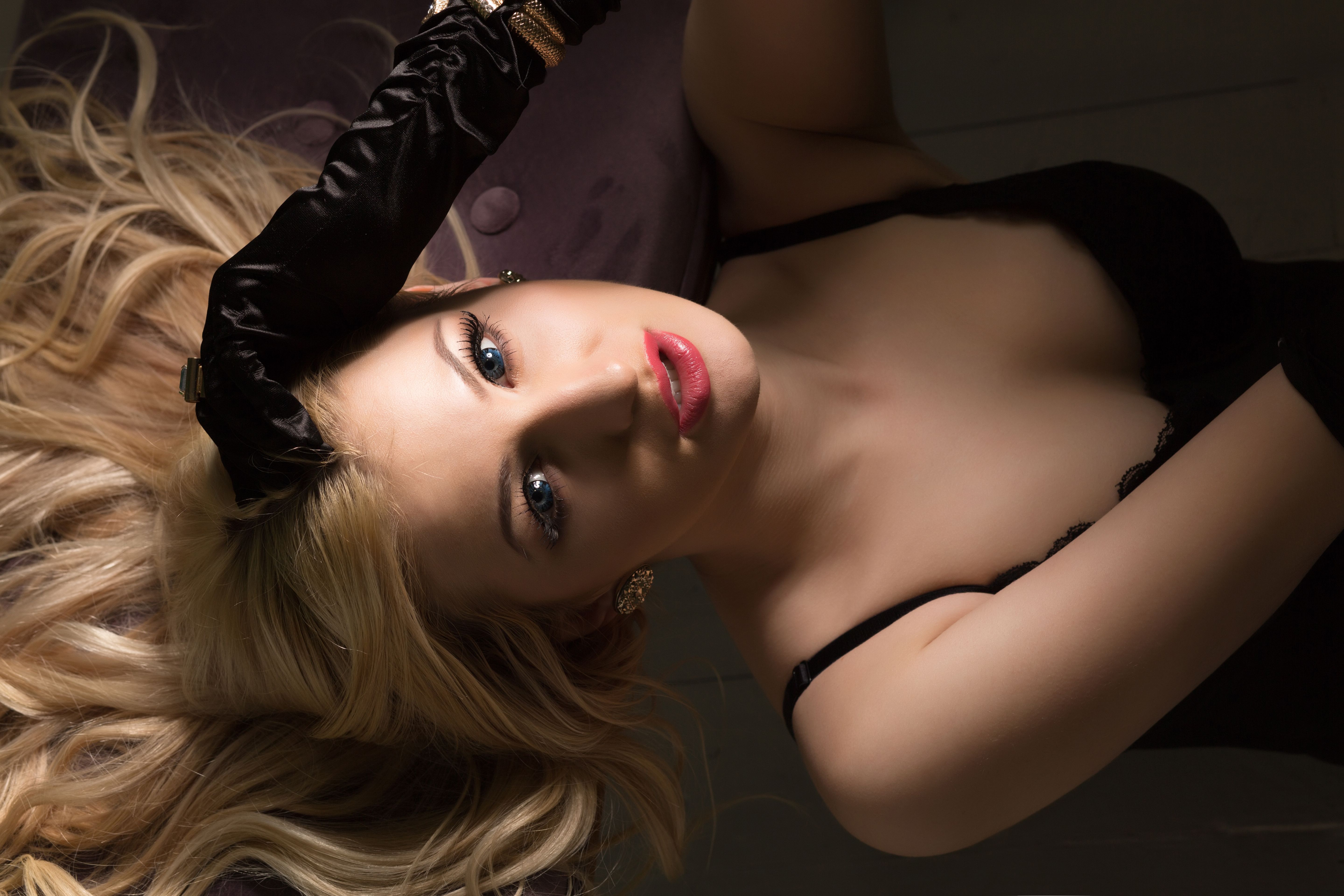 Seductive blonde woman in sexy black lingerie and silk gloves posing in the dark
