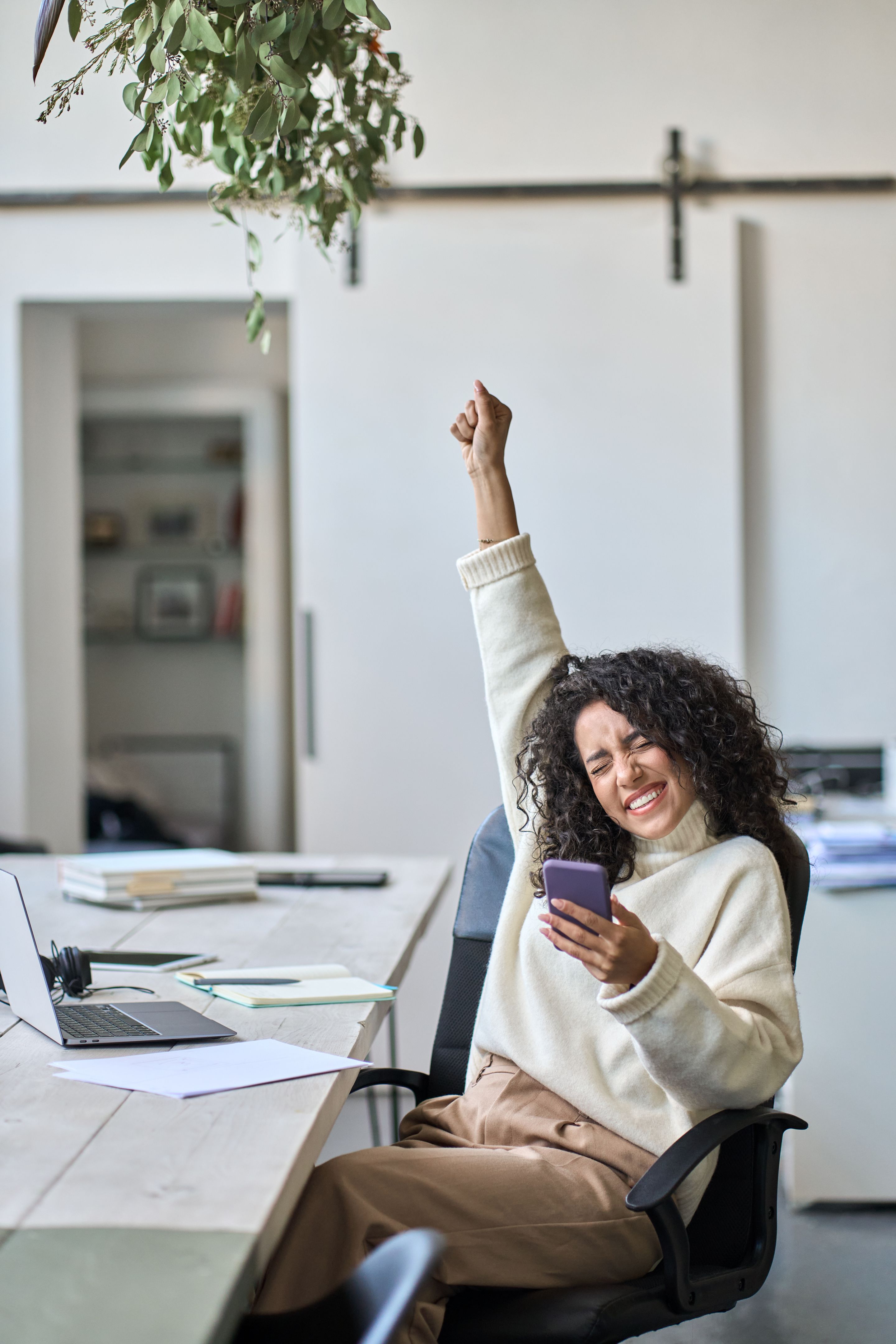 Euphoric young female worker holding mobile phone celebrating win.