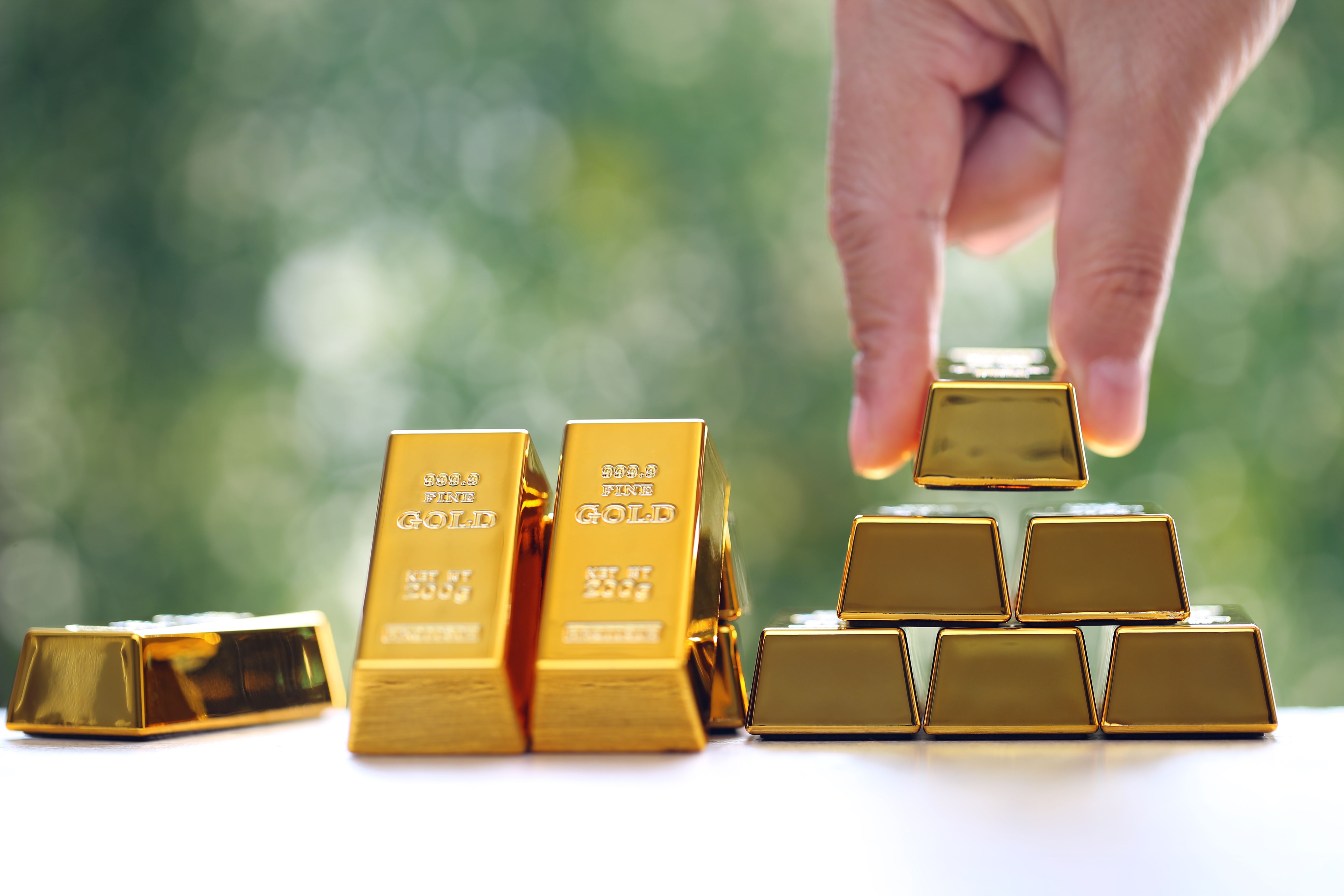 Woman hand hold the gold bar on natural green background, investment and business concept