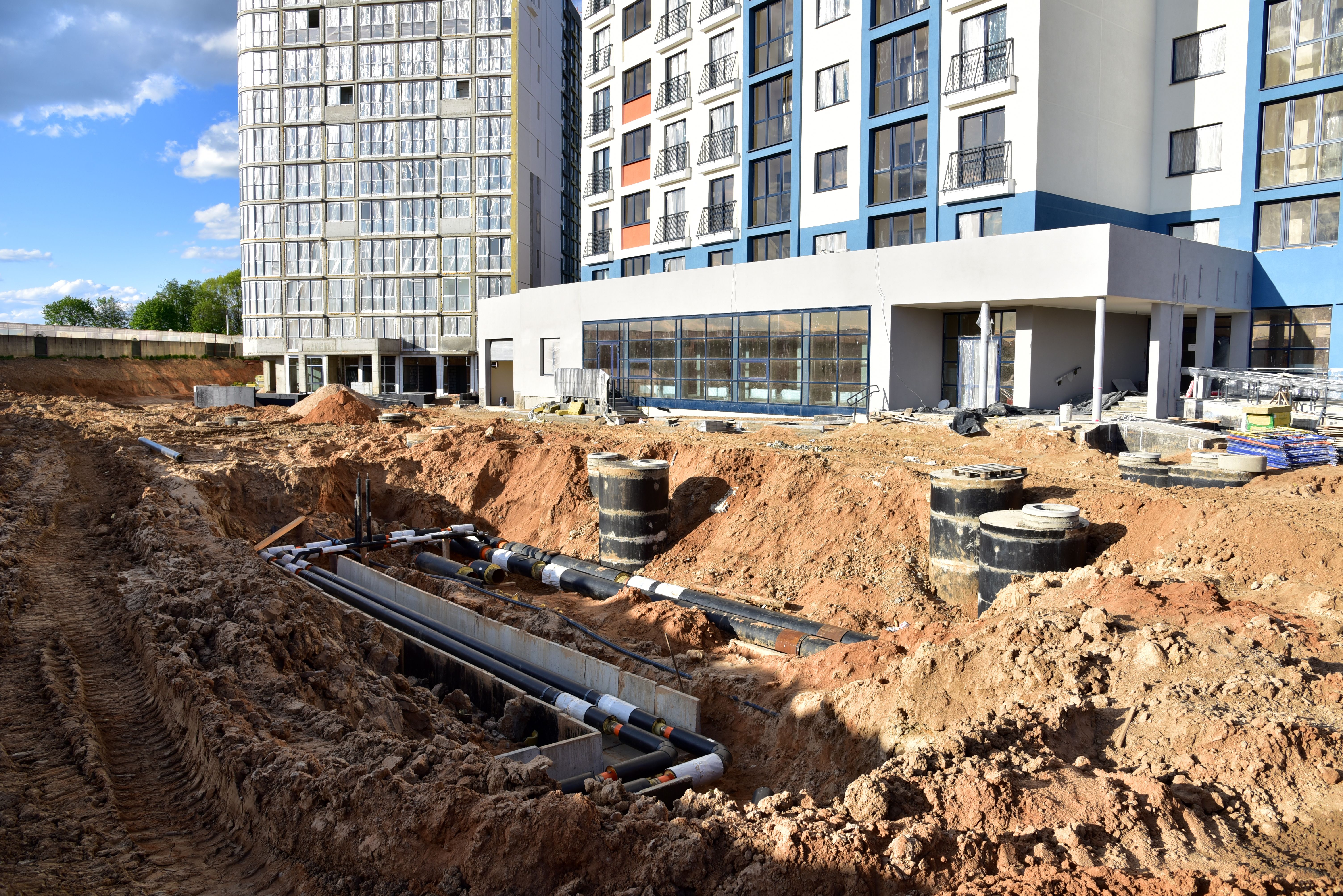 Laying heating pipes in trench at construction site. Installing concrete sewer wells and underground storm systems of sanitary water main. Cold and hot water heating system of the apartments in house Laying heating pipes in trench at construction site. Installing concrete sewer wells and underground storm systems of sanitary water main. Cold and hot water heating system of the apartments in house