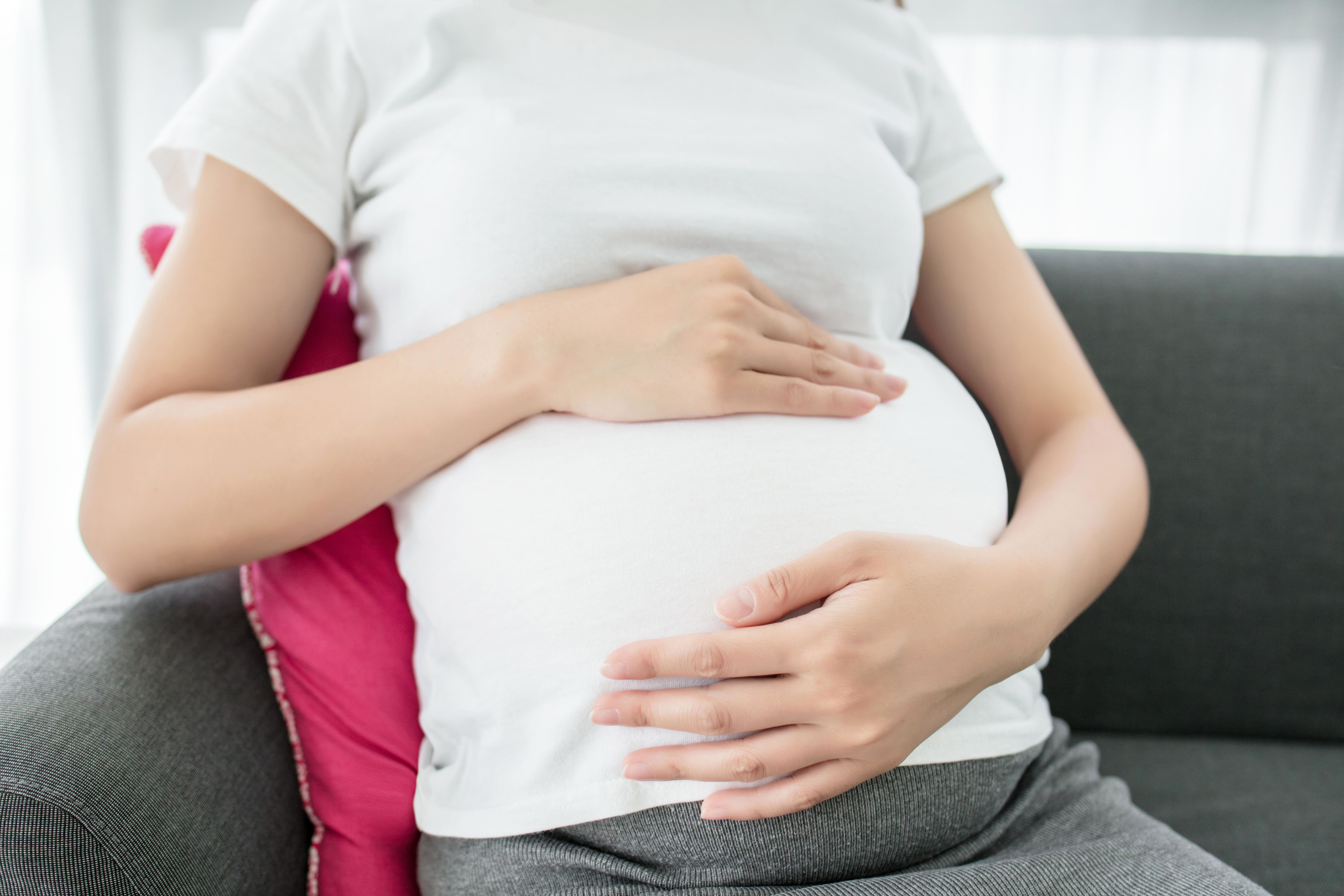 Pregnant woman sitting on sofa and touching her belly