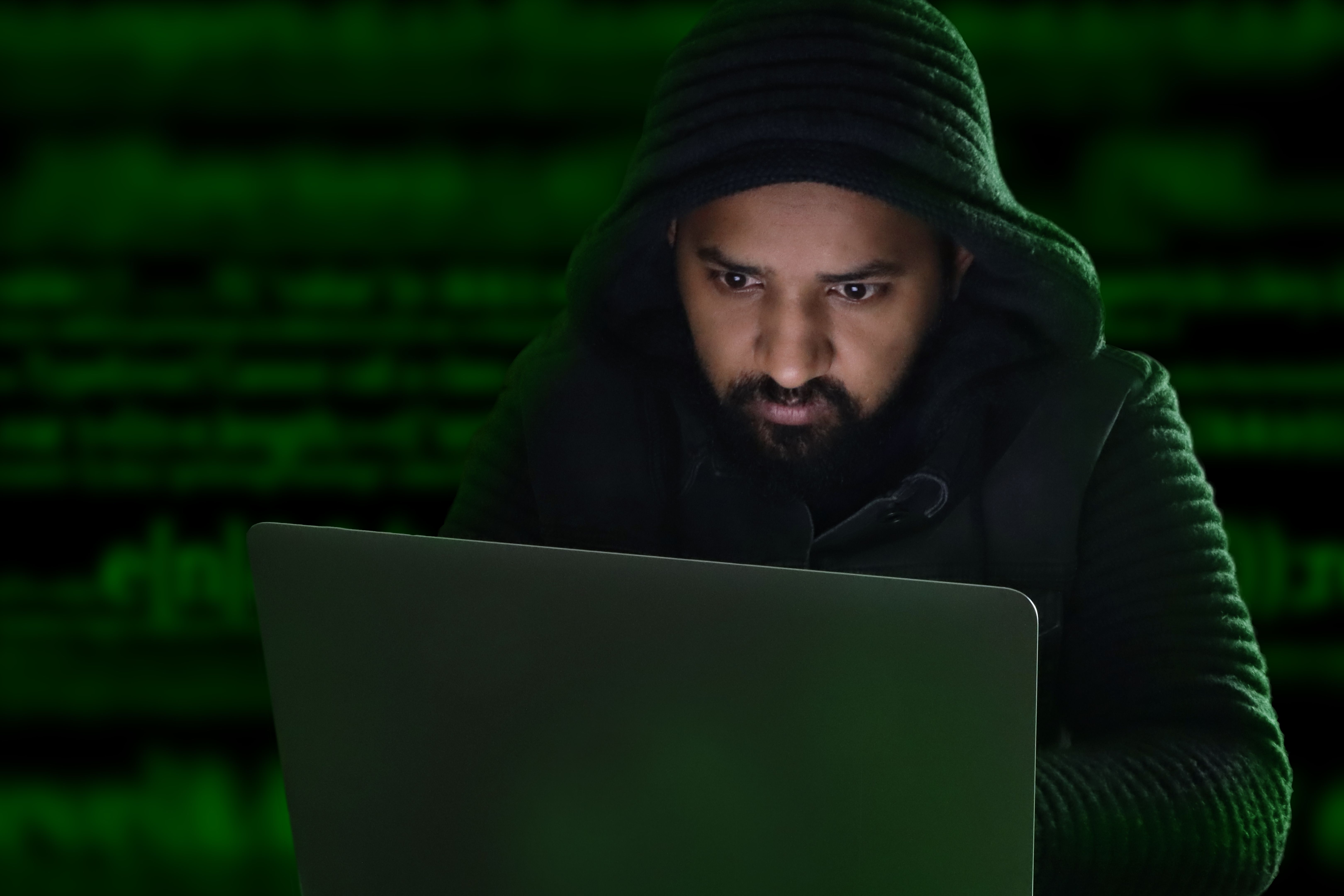Image of male, asian computer hacker / programmer wearing hoodie with dark programming computer code background, Internet crime concept Image of male, asian computer hacker / programmer wearing hoodie with dark programming computer code background, Internet crime concept