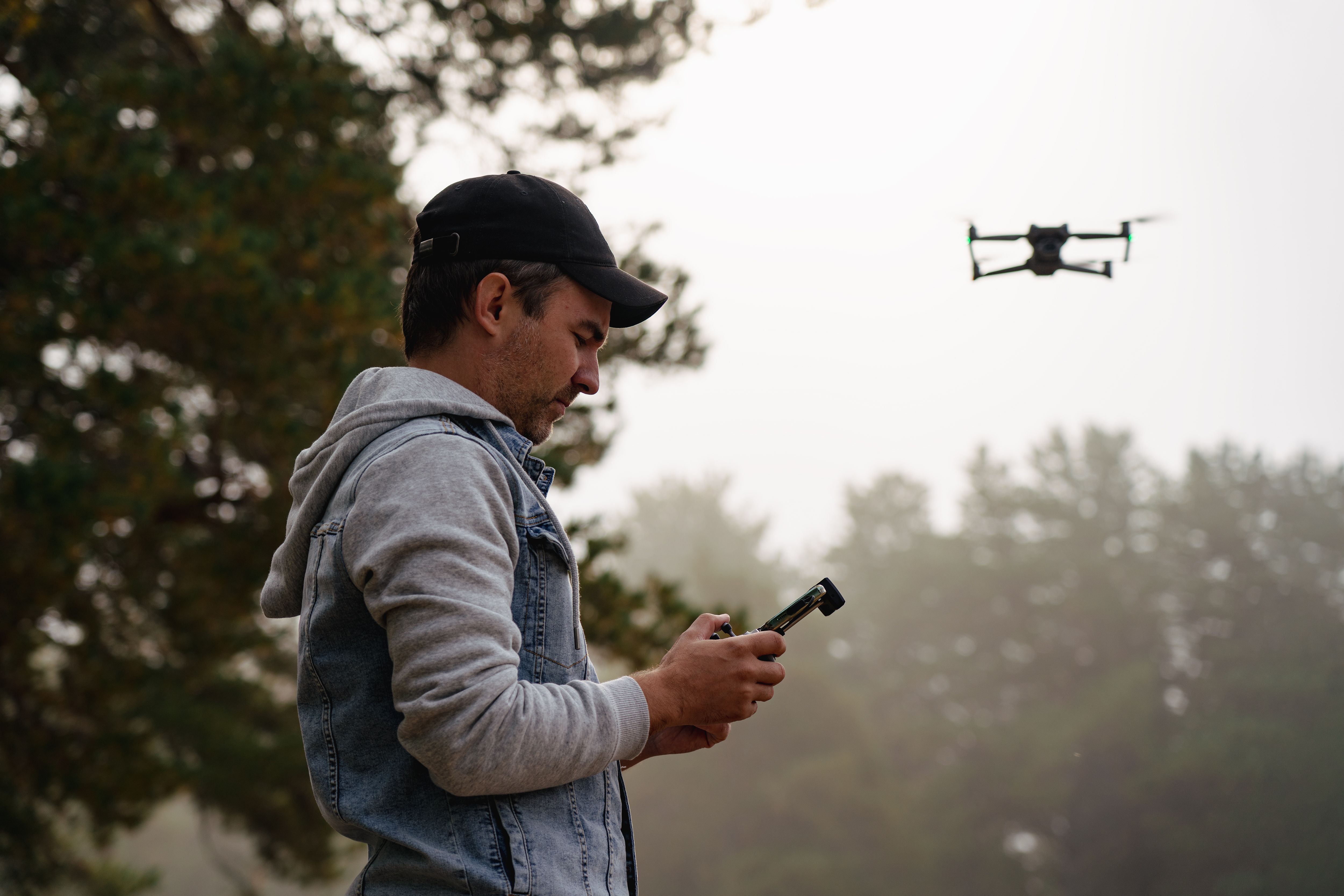 Professional photographer taking photos from drone. Young man taking aerial photos in forest. Man controlling his drone on background of mountain forest.
