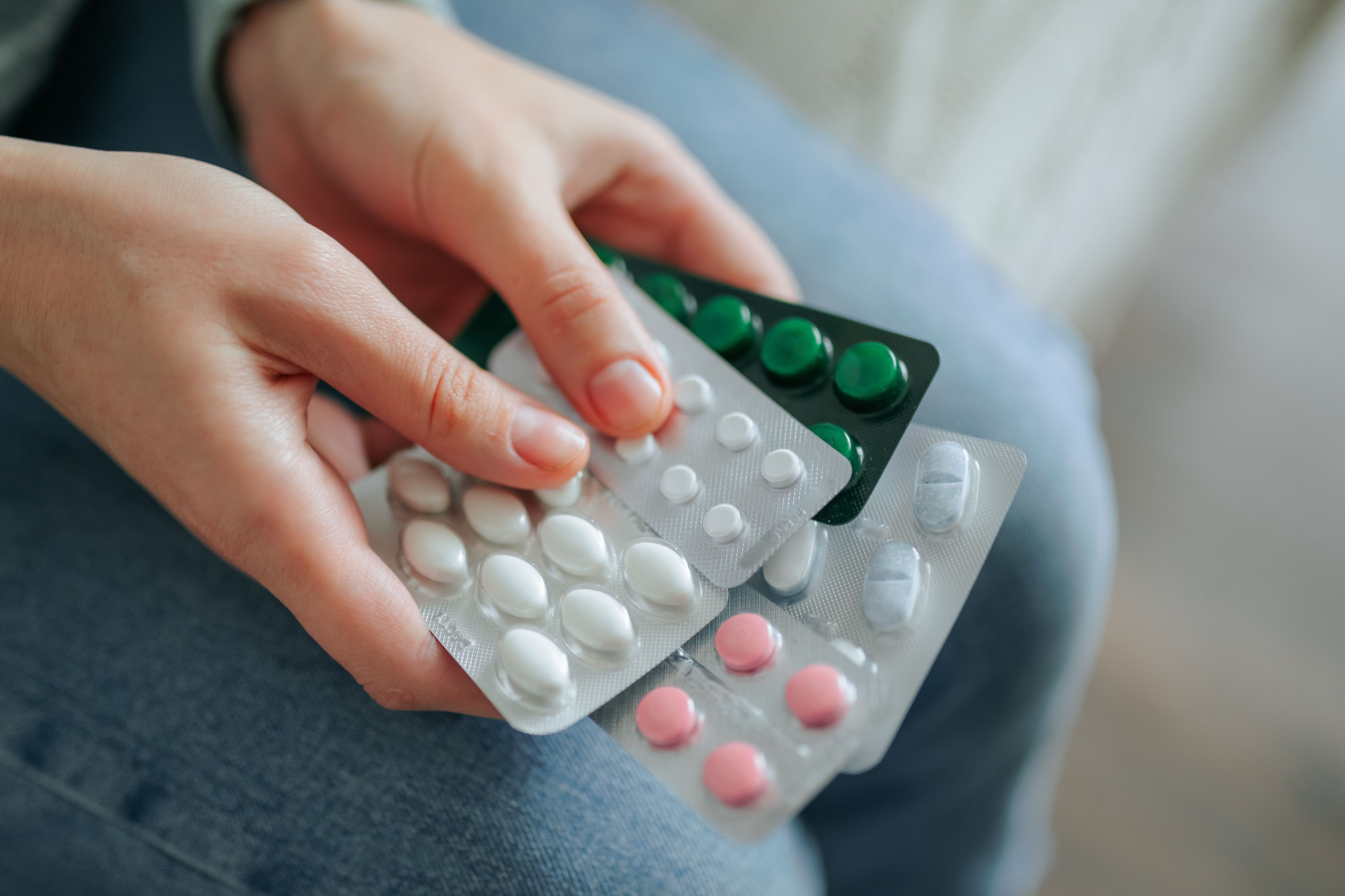 Hands holding multiple blister packs of medication in a casual setting