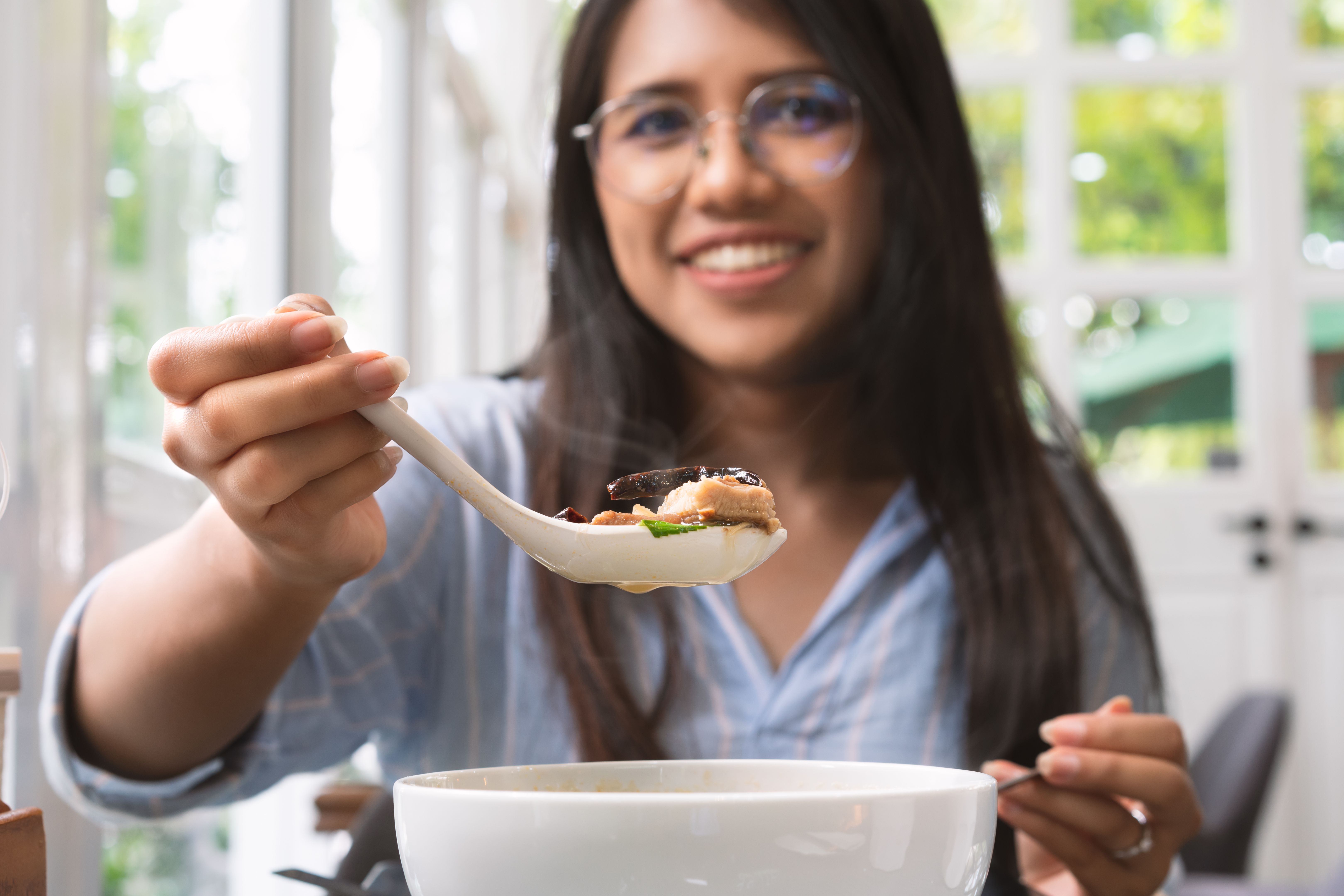 Asian woman holding up a spoon of Thai food to the camera in a trendy cafe