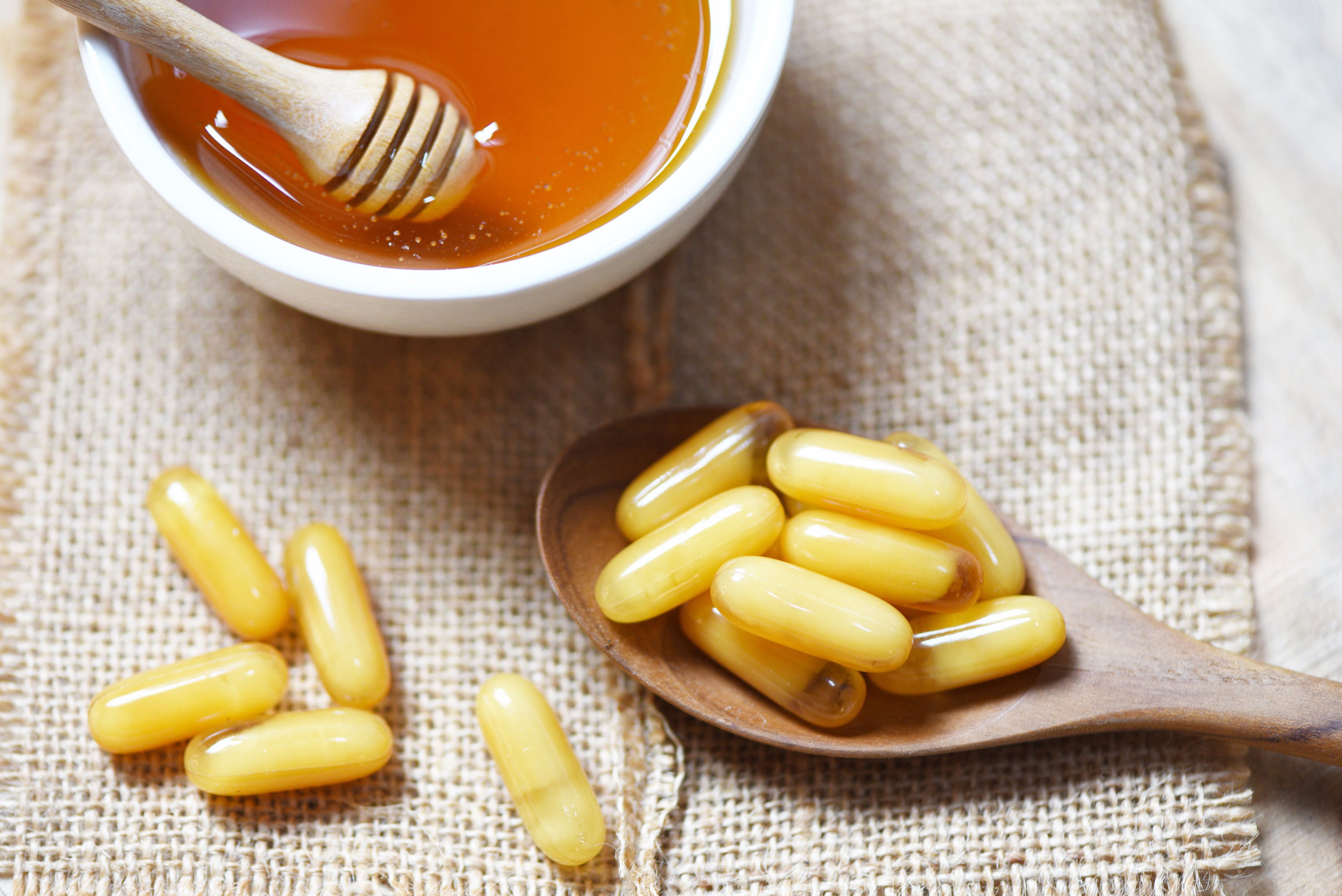 Royal jelly capsules in wooden spoon on sack background and honey in cup - Yellow capsule medicine or supplementary food from nature for health