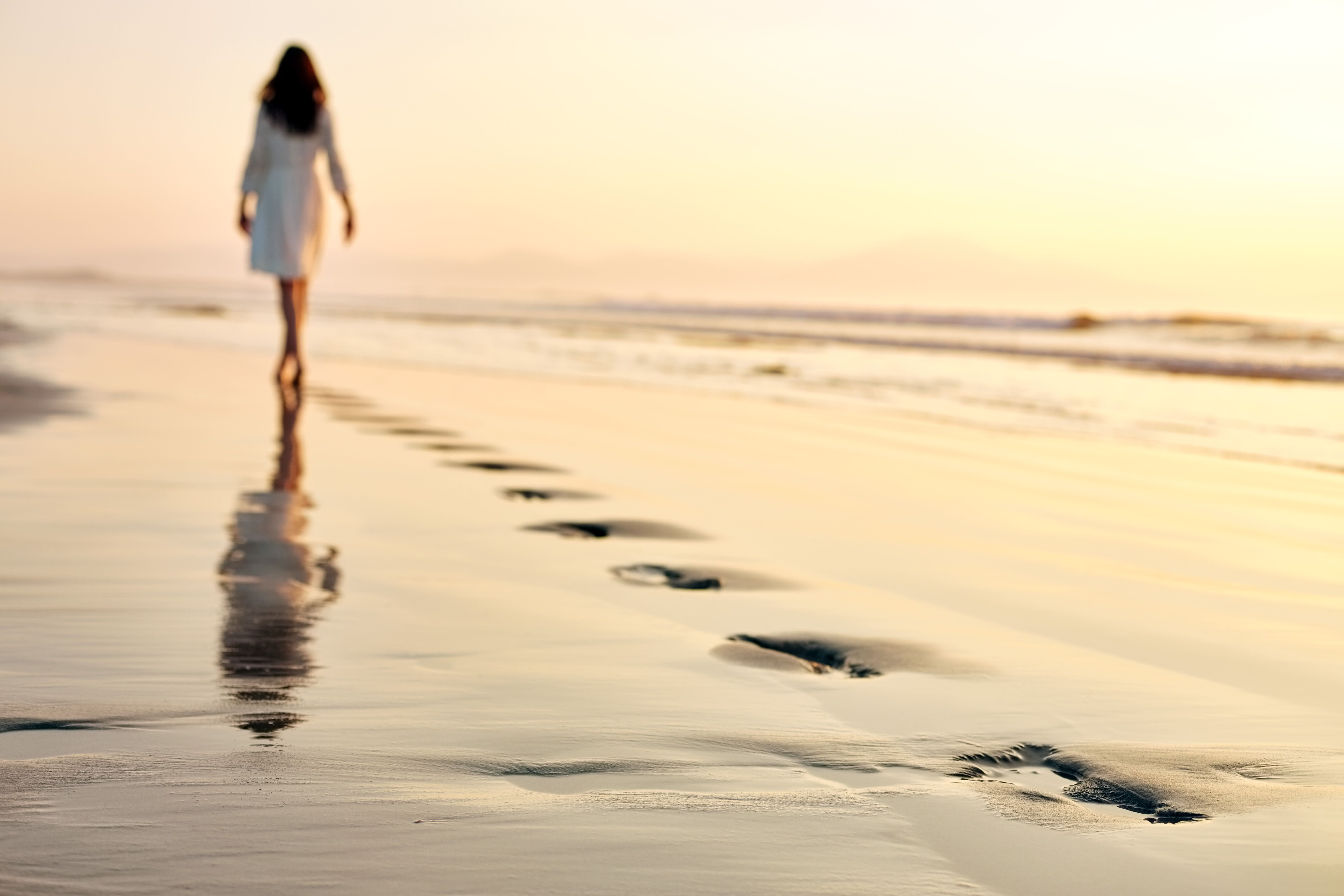 Woman leaving footprints while walking on wet sand at sunset Woman leaving footprints while walking on wet sand at sunset