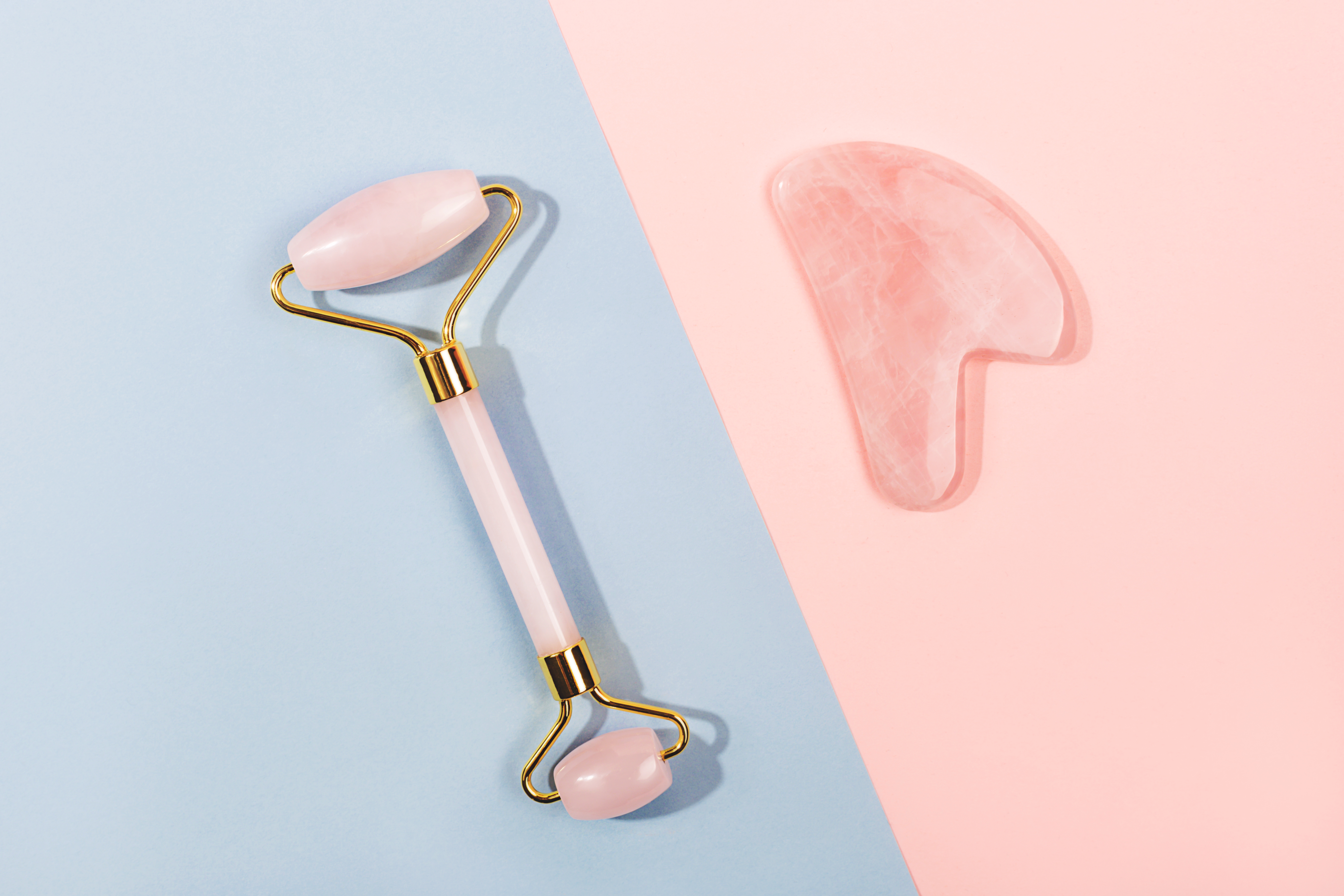 Pink jade roller and gua sha tool on pastel background.