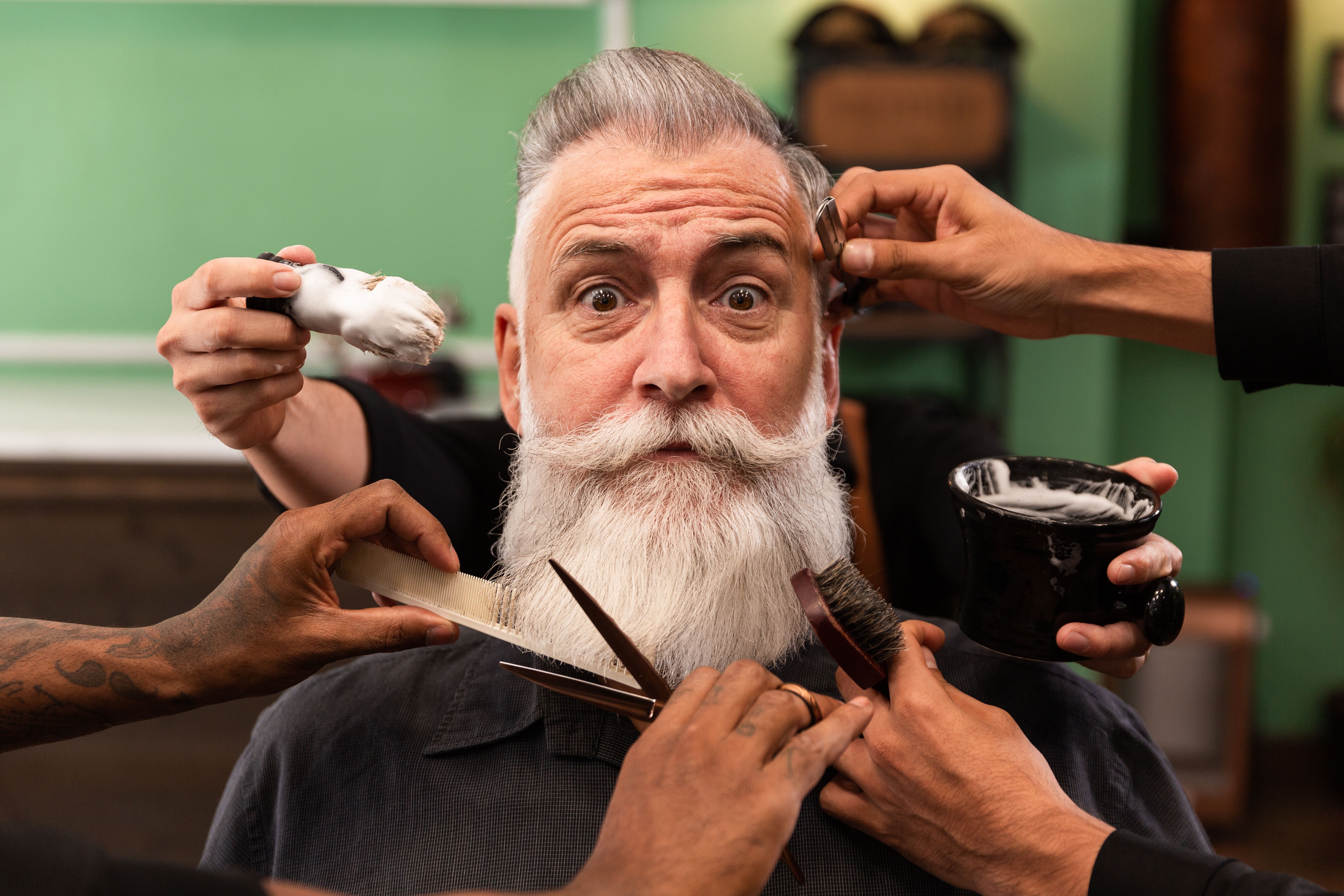 homem com barba branca na barbearia com mãos de barbeiro com instrumentos de corte e barbear