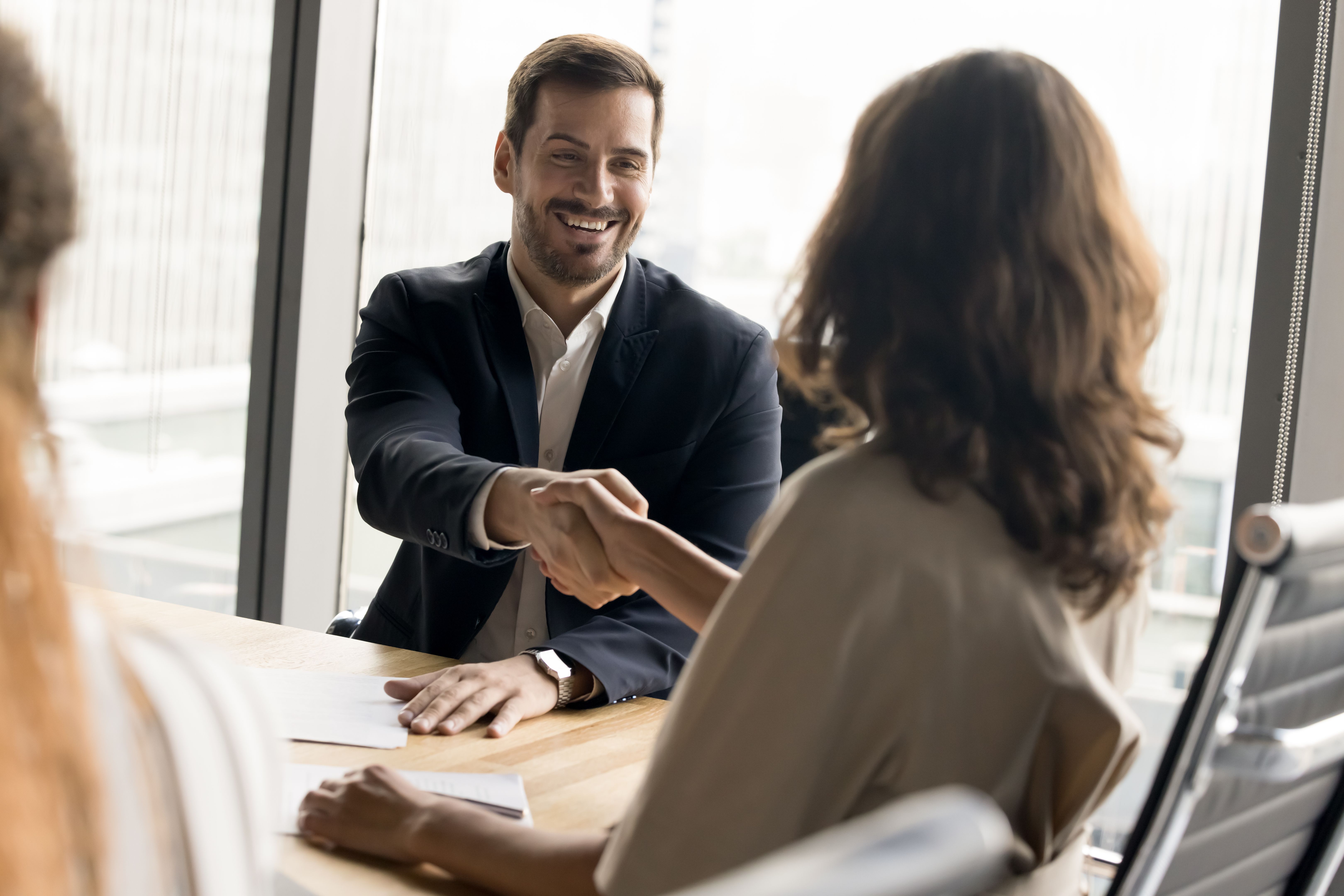 Positive millennial business partners shaking hands on corporate meeting