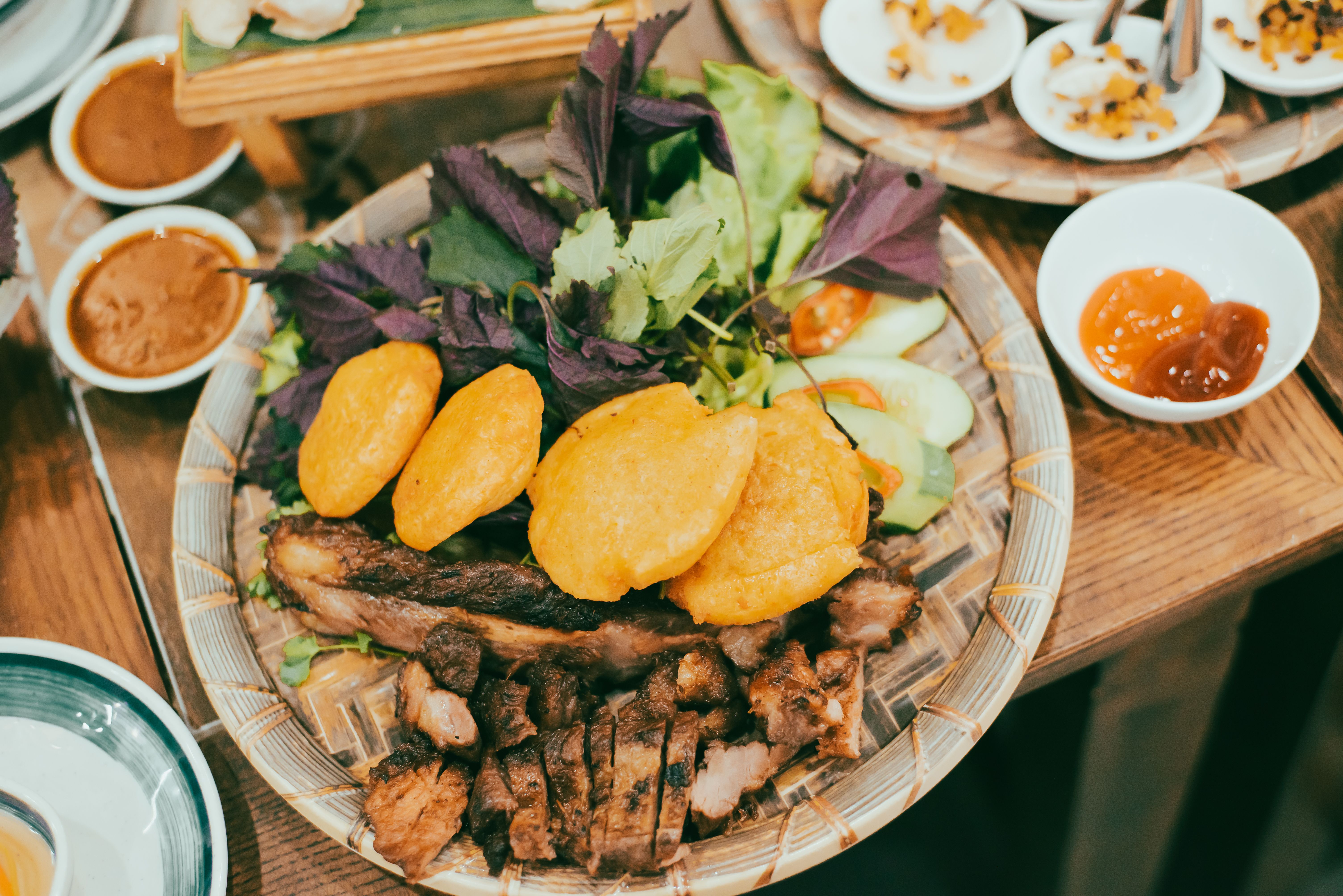 Top view balanced eating Hue Vietnam dinner set of crispy fried dough with grilled pork, cucumber slides, herbs, various vegetables on bamboo mat and dipping sauce, local authentic cuisine